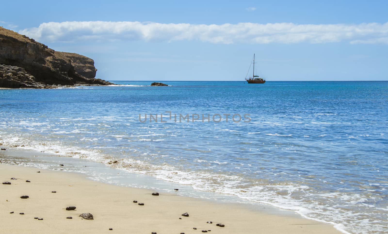 Lonely beach with volcanic dark stones. Blue sky and a dark cliff on the background