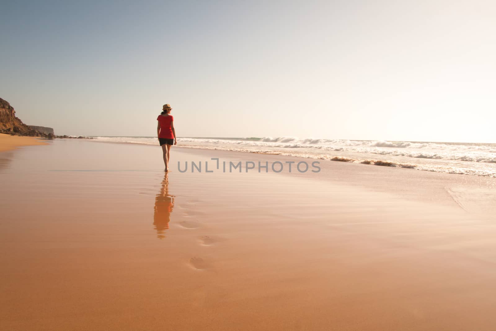 Solitary girl on beach looking at the sea with her reflection. Sunset time.