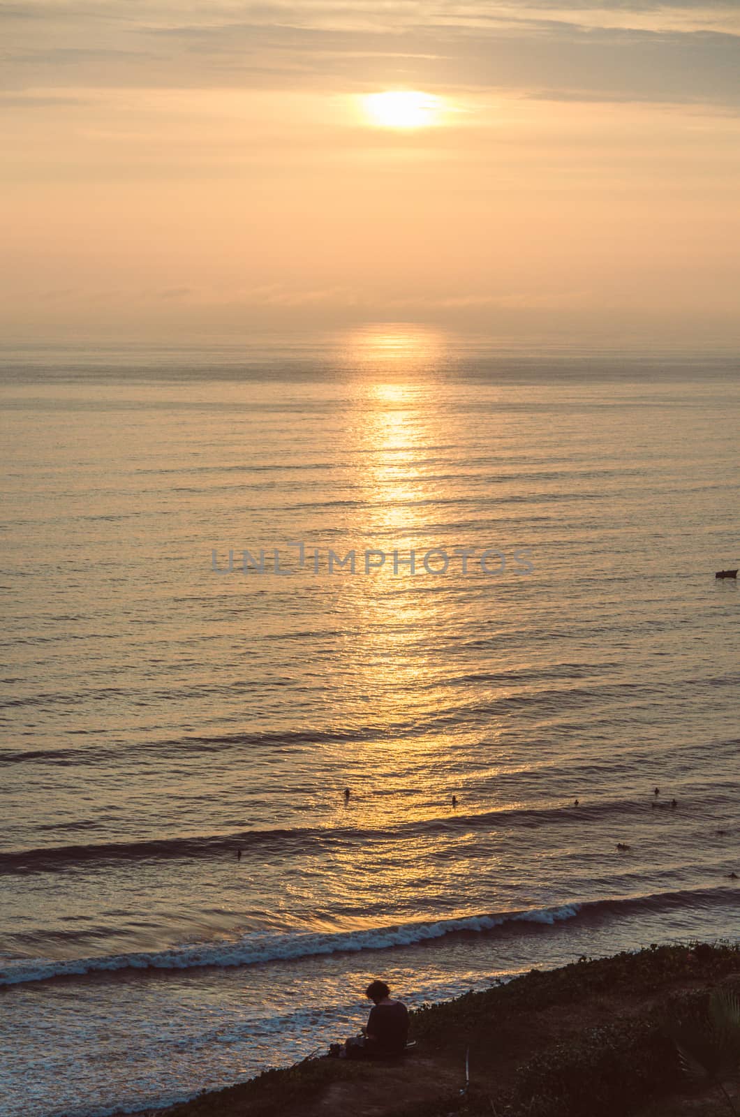 Man sitting at the foot of the sea watching the sunset