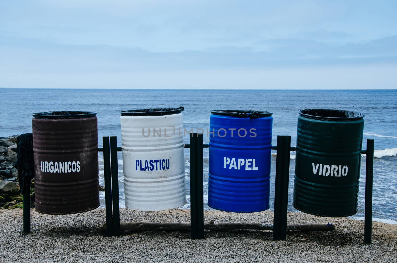 Recycling bins of different colors on the beach that says: organic = organic, plastic = plastic, paper = paper, vidrio = glass