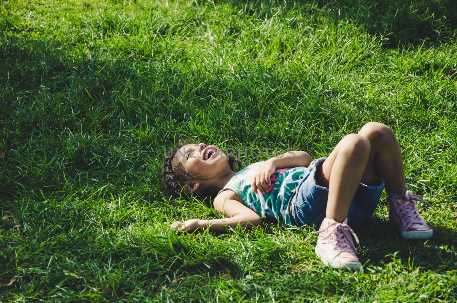 Laughing little girl lying on the grass in the park