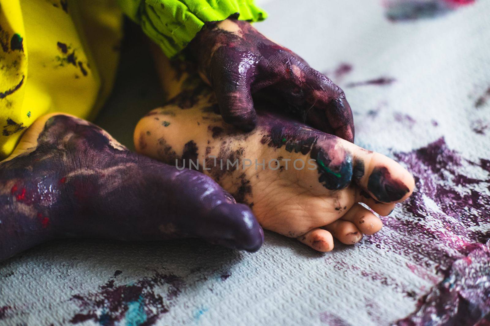 Chlid playing with different color paintings ends with multicolor hands and feet