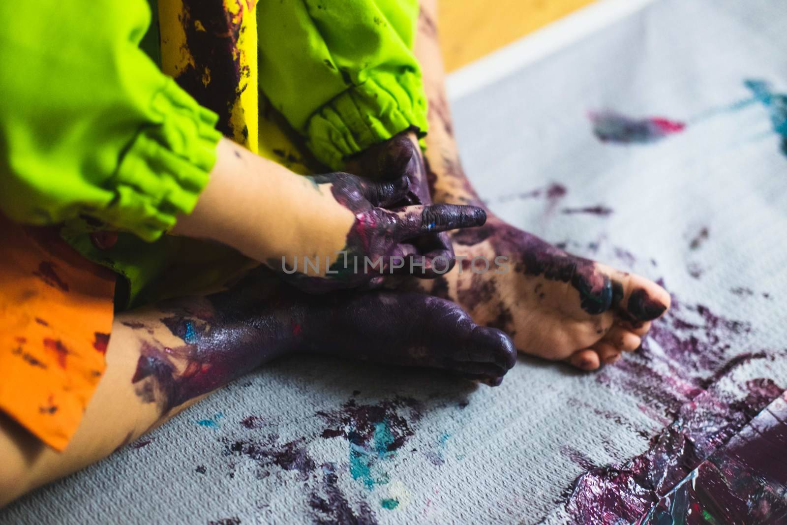 Chlid playing with different color paintings ends with multicolor hands and feet