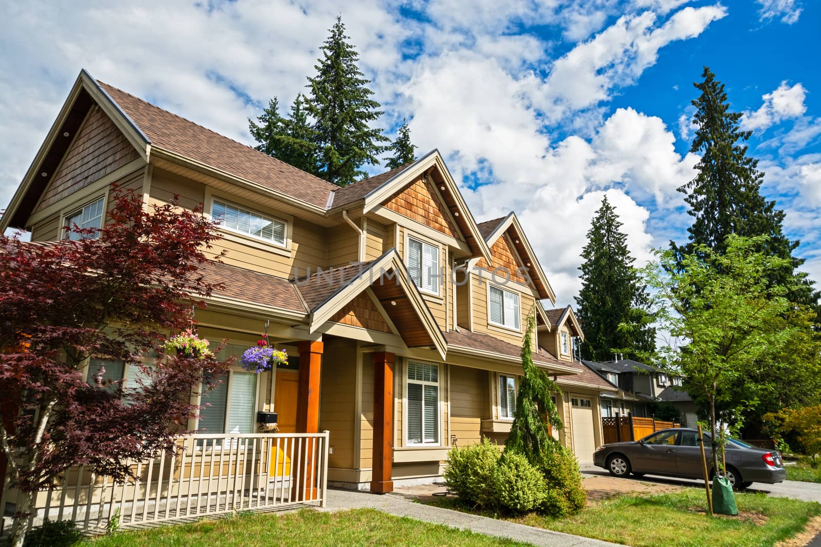 Luxury residential house with car parked in front on cloudy sky background.