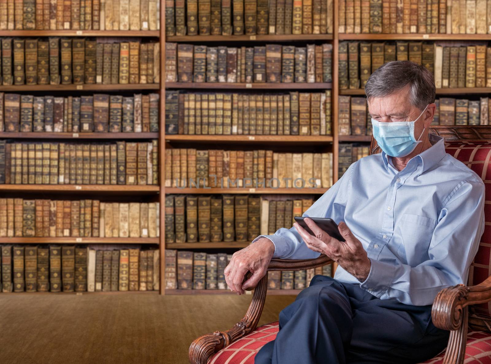 Senior man in face mask against virus reading ebook in antique library by steheap
