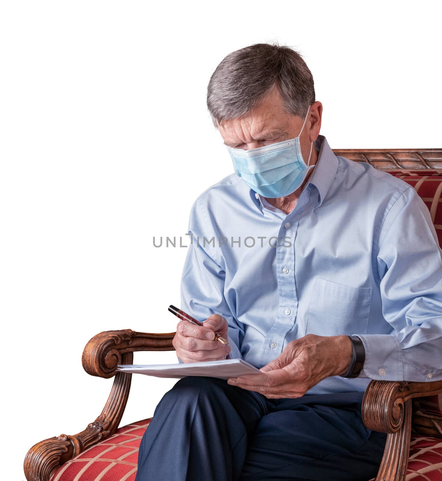 Senior caucasian adult checking a document in hand while seated. He is wearing a face mask against coronavirus and cutout against white