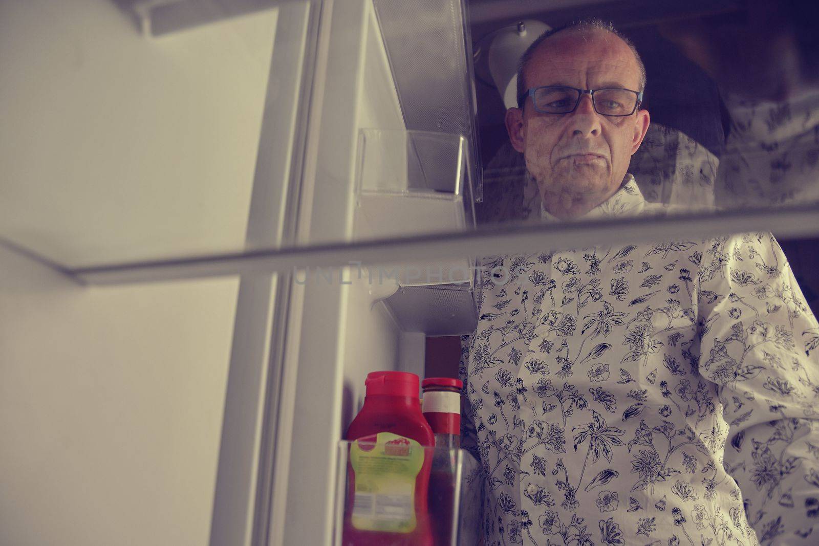 Hungry man looking for a late night meal in an empty fridge. Tired old man looking for a snack in the fridge at night, view from the fridge.