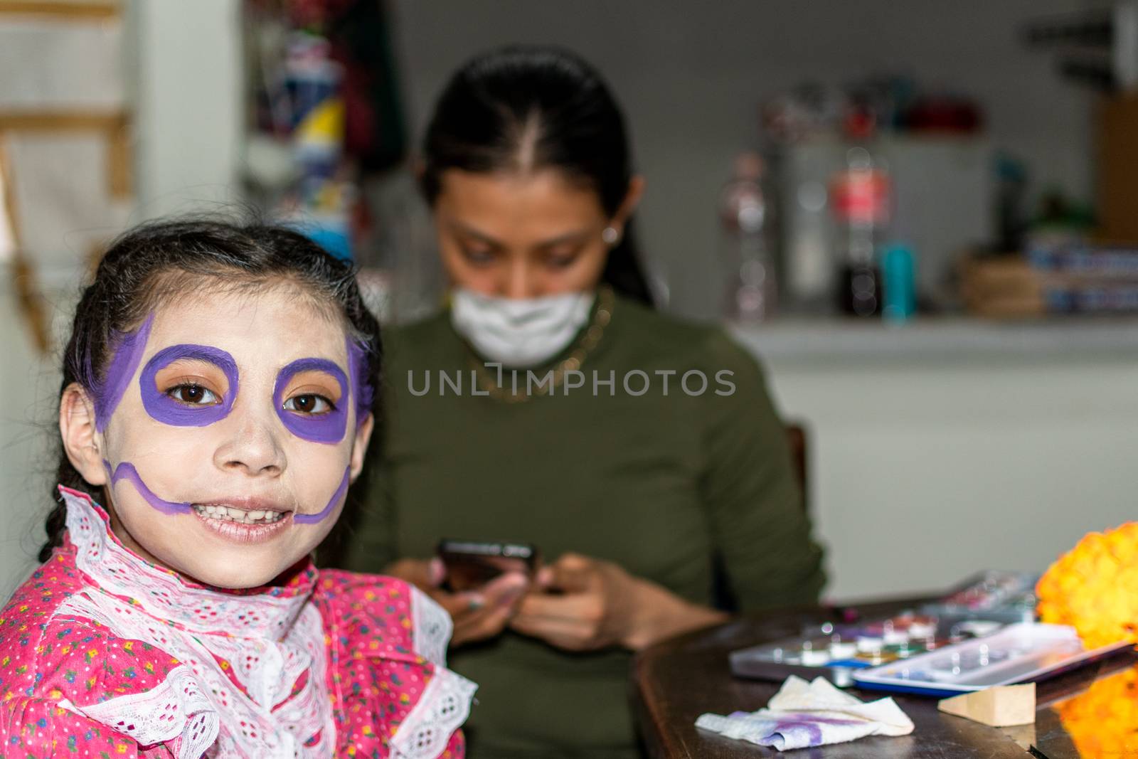 mother putting makeup of Catrina on her daughter's face to celebrate a festival