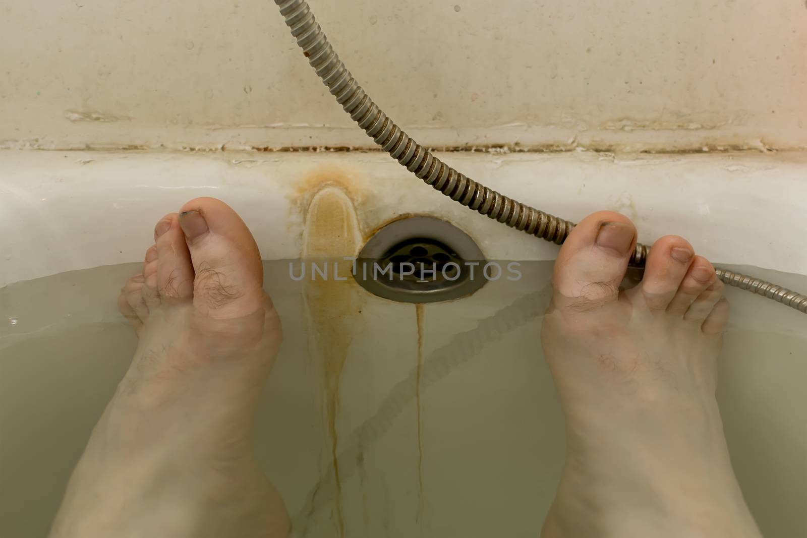 human feet in the water in the dirty rusty bath of a communal apartment, unsanitary conditions, poor living conditions