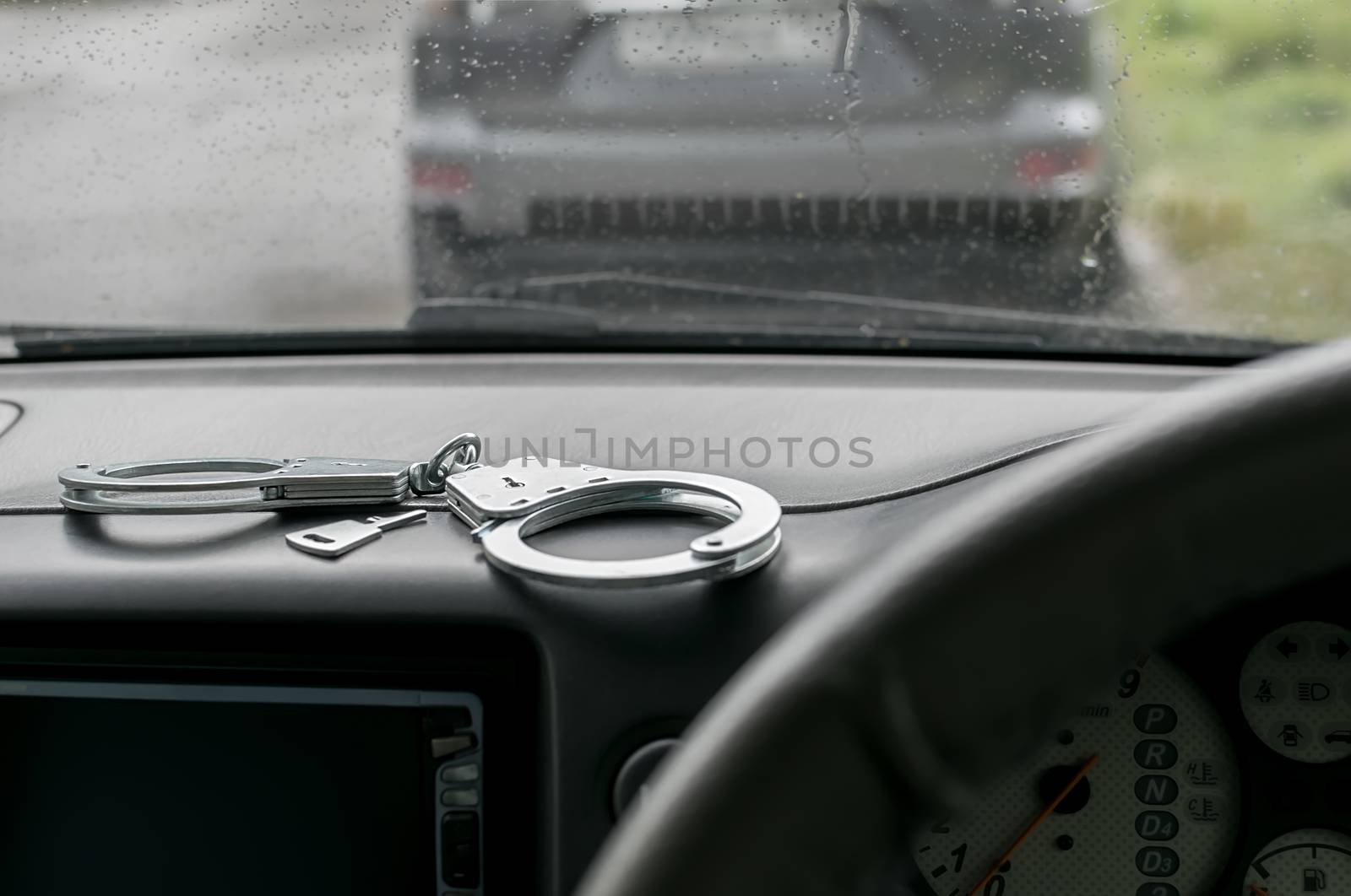 metal handcuffs lie on the dashboard of the car against the rain soaked windscreen