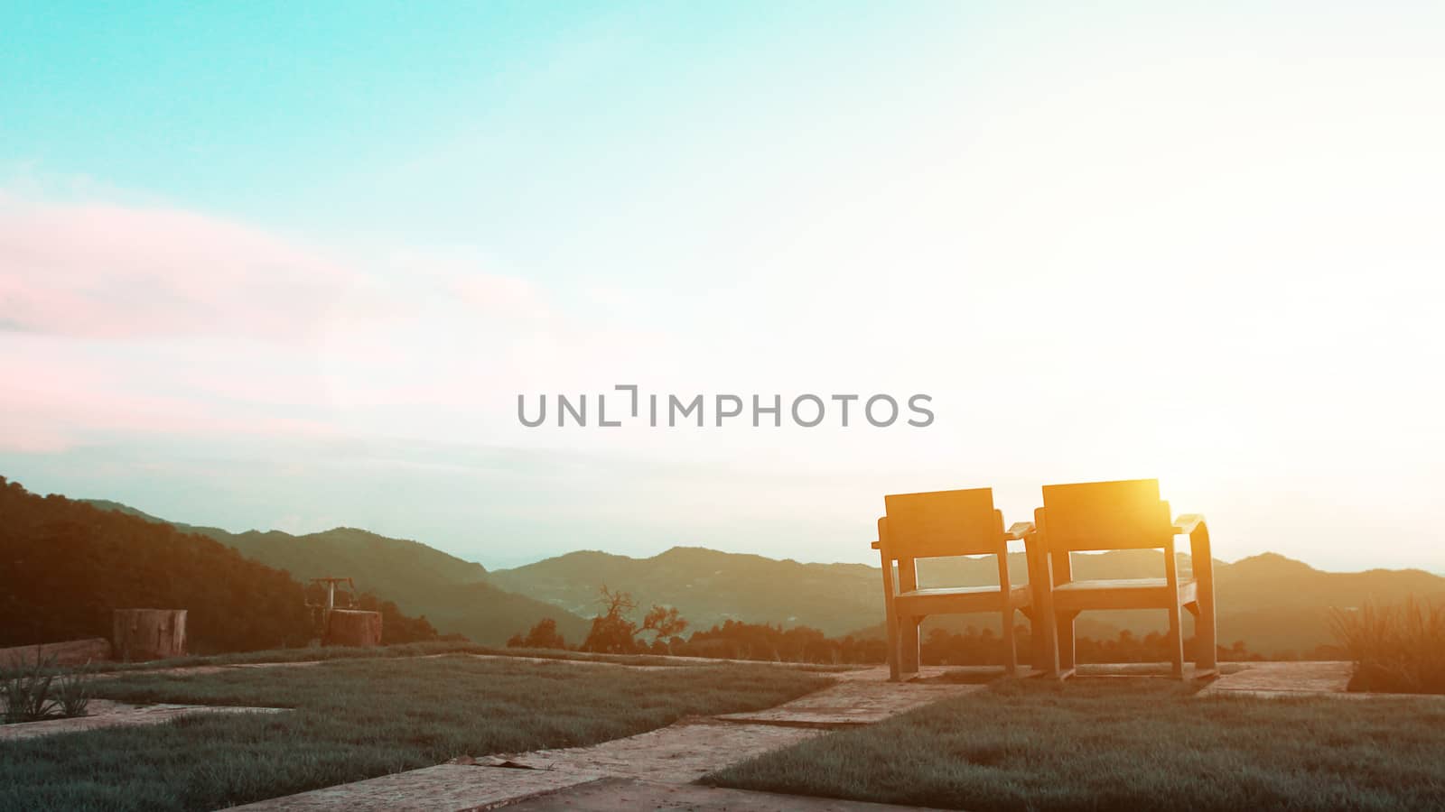 Two wooden comfortable chairs sitting in the yard facing a mountain nature view. Across the calm forest with green trees and sun light in the morning. Relax vacation concept for slow life background