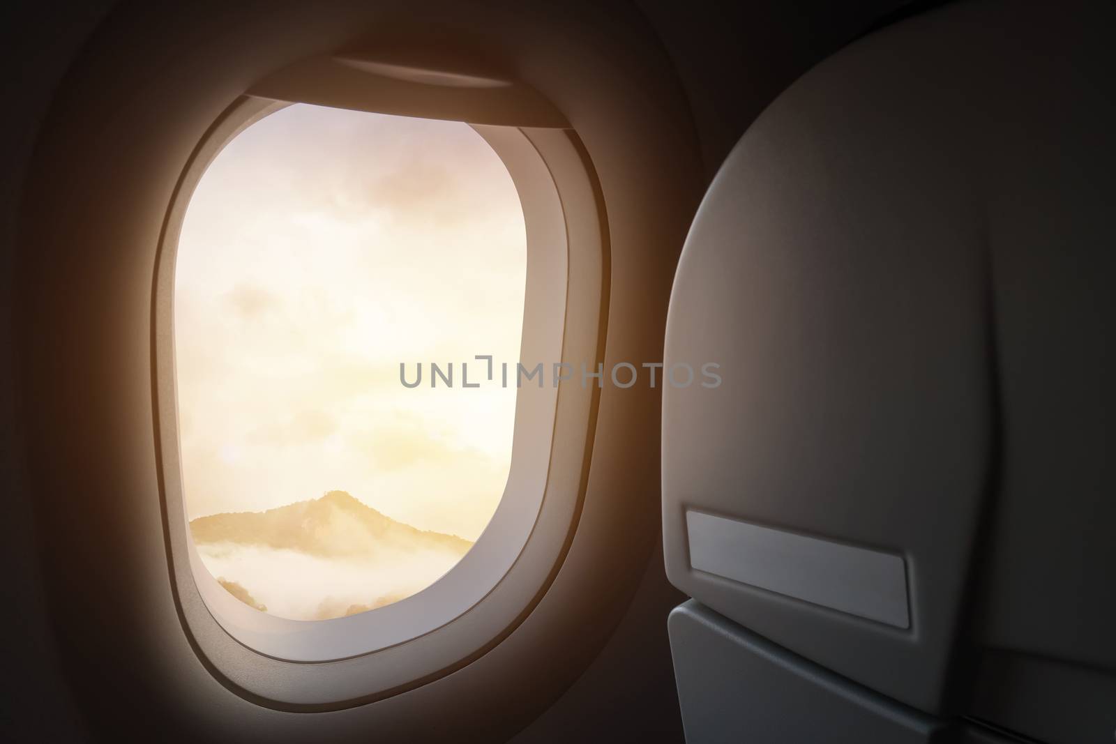 travel and journey by plane concept. view of beautiful mountain and fog with golden sunlight and lens flare as seen through window of an aircraft