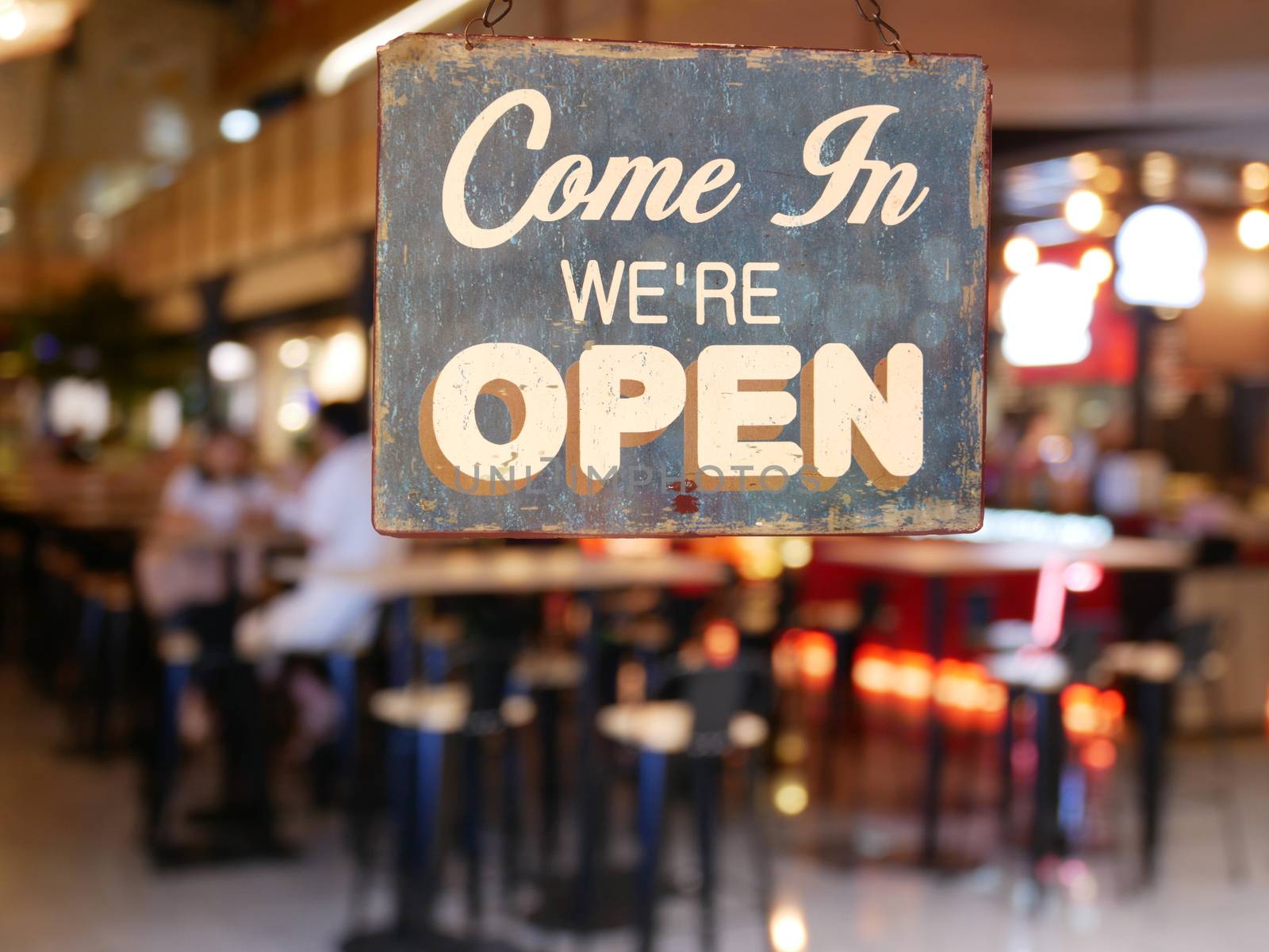 A business vintage sign that says 'Come in We're Open' on Cafe / Restaurant window. Image of abstract blur restaurant with people. Restaurant with customer for background usage