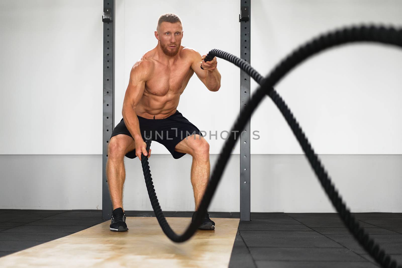 Gym battle rope man stamina training Athlete guy fitness exercising endurance indoor workout. by andreonegin