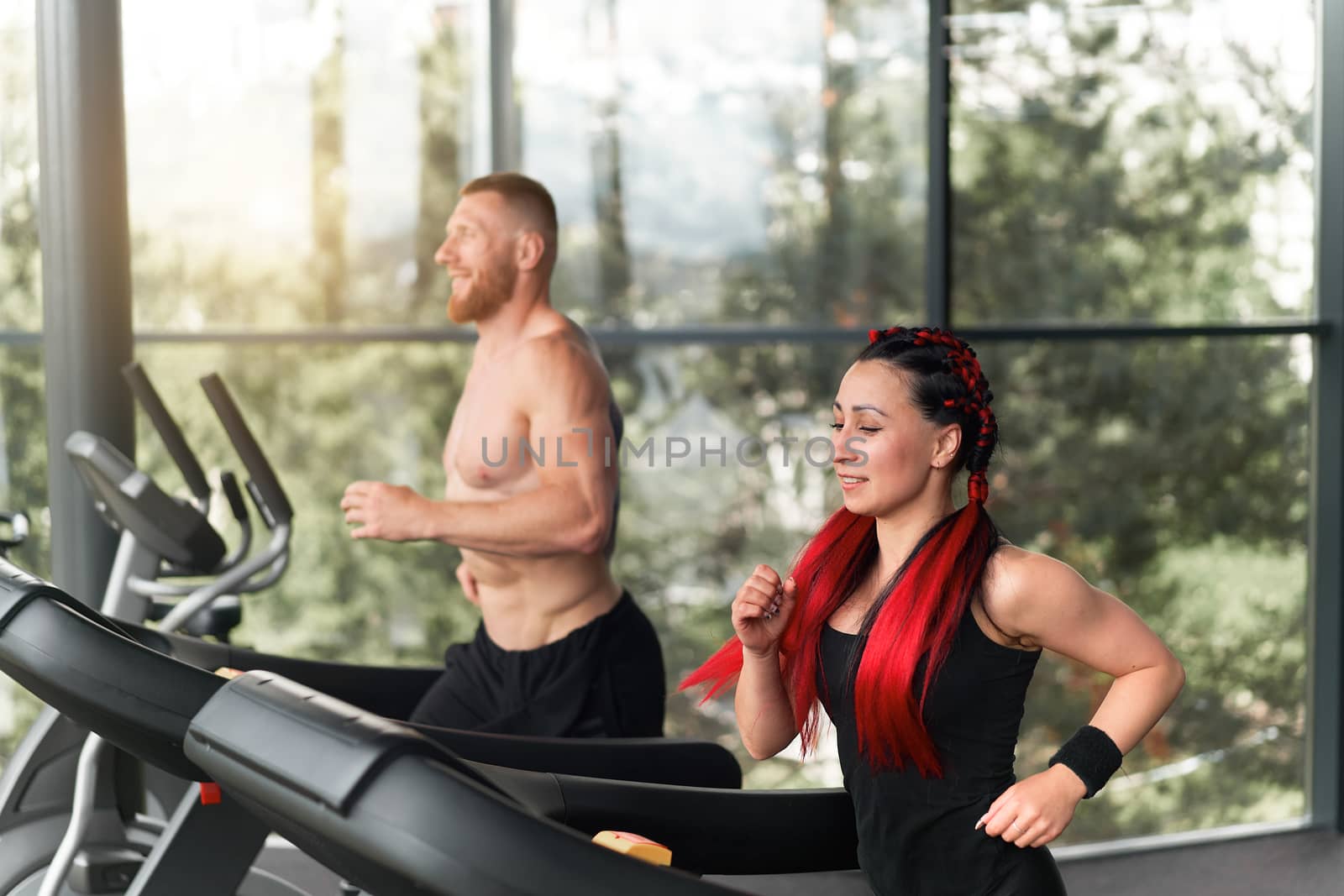 Gym treadmill running trainer man woman training together jogging fitness workout Warming up before functional cross training Personal coach train girl run on treadmil with panoramic window background