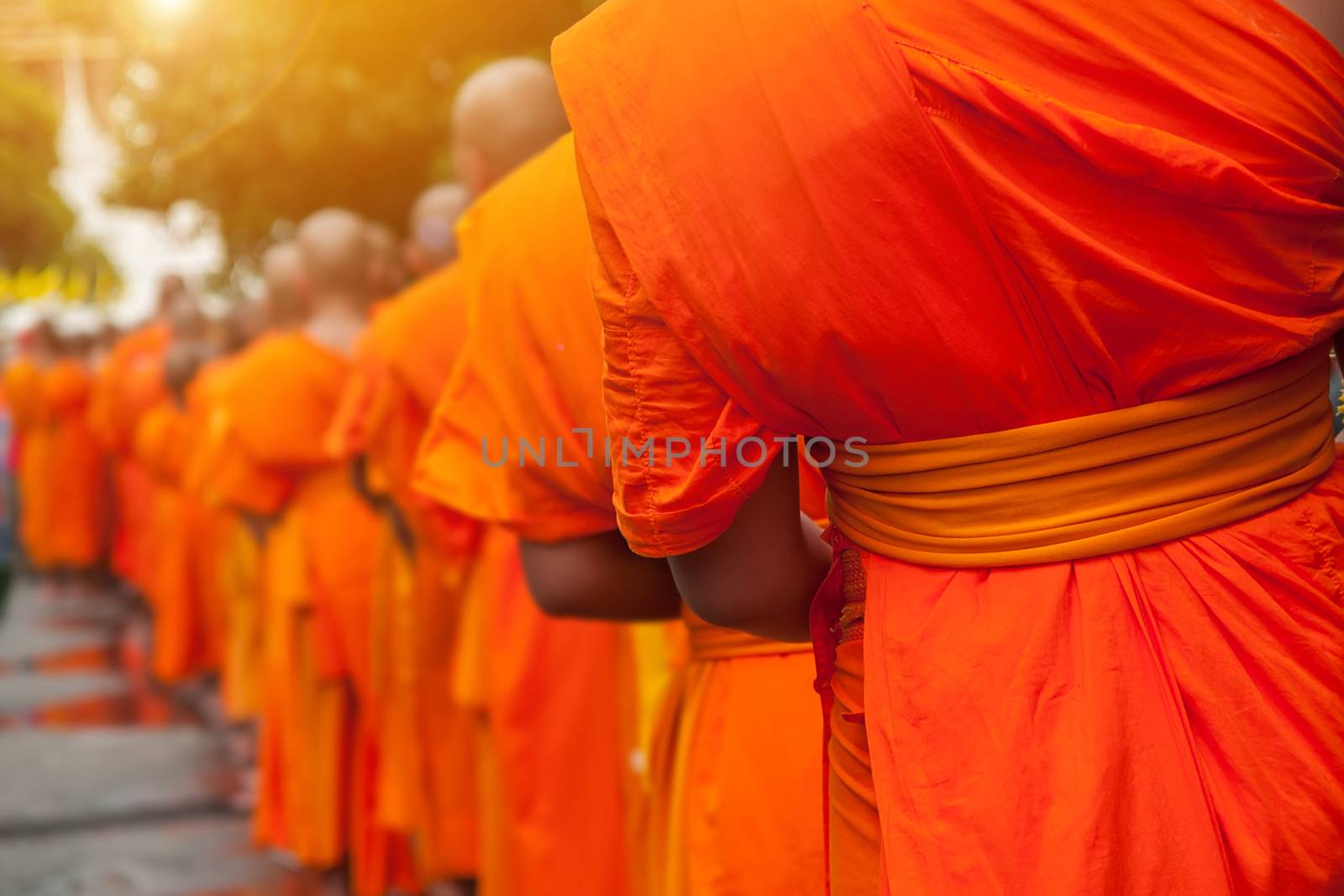 Buddhist philanthropy concept. Buddhist Monks line up in row waiting for Buddhism people to give alms bowl in Thai temple at morning time. Selective focus at front Monk. Light with len flare effect