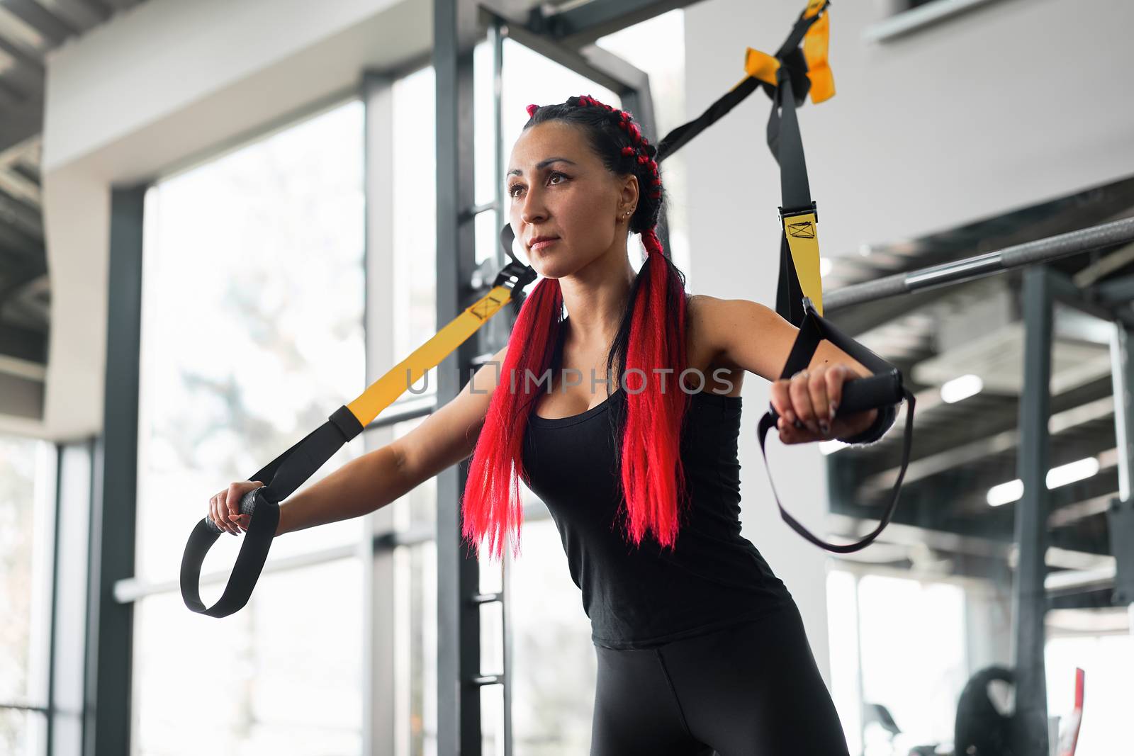 Athlete woman training exercising with suspension system indoor gym. Beautiful caucasian sportive woman do stretching strenght exercise with special strap by andreonegin
