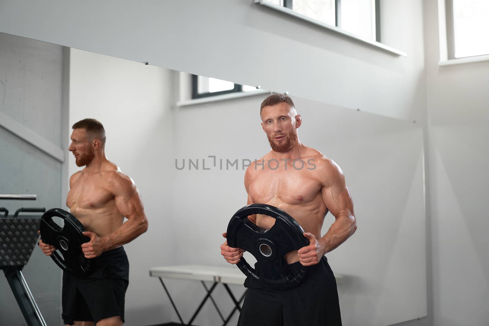 Athlete sportive man gym Middle adult handsome sportsman bodybuilder weightlifter ideal body after training Caucasian trainer standing naked torso With barbell plates in hand mirror background