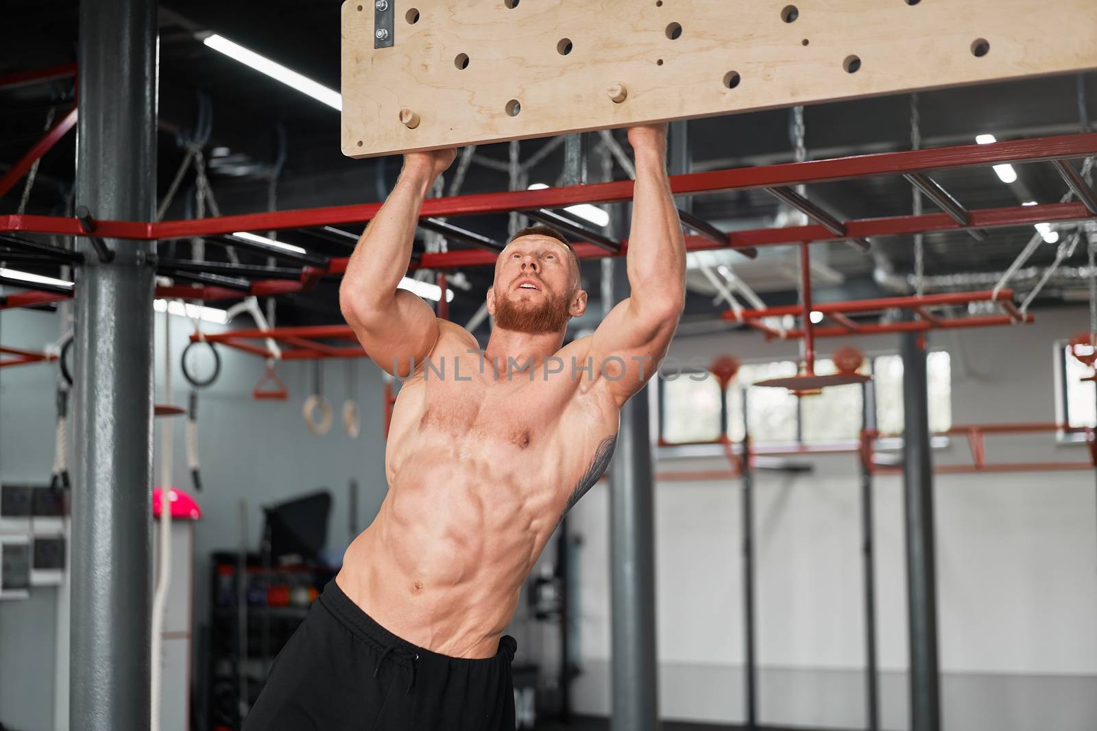 Man climbing pegboard gym athlete training arm strength stamina alpinism indoor. Athlete caucasian guy hanging from his hands wooden campus board warming up to climb Functional Cross training workout