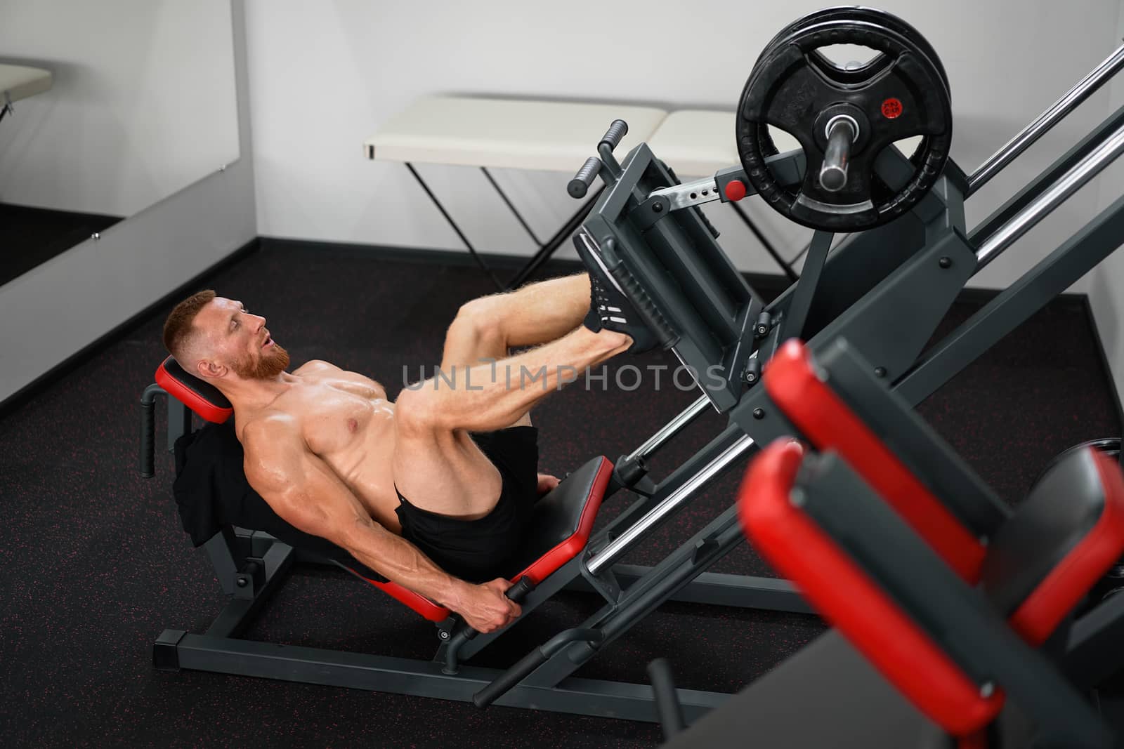 Gym man leg press machine training pushing weight Handsome caucasian guy training define his upper legs muscule Bodybuilder cross training indoors. Make your body. Naked torso shirtless.