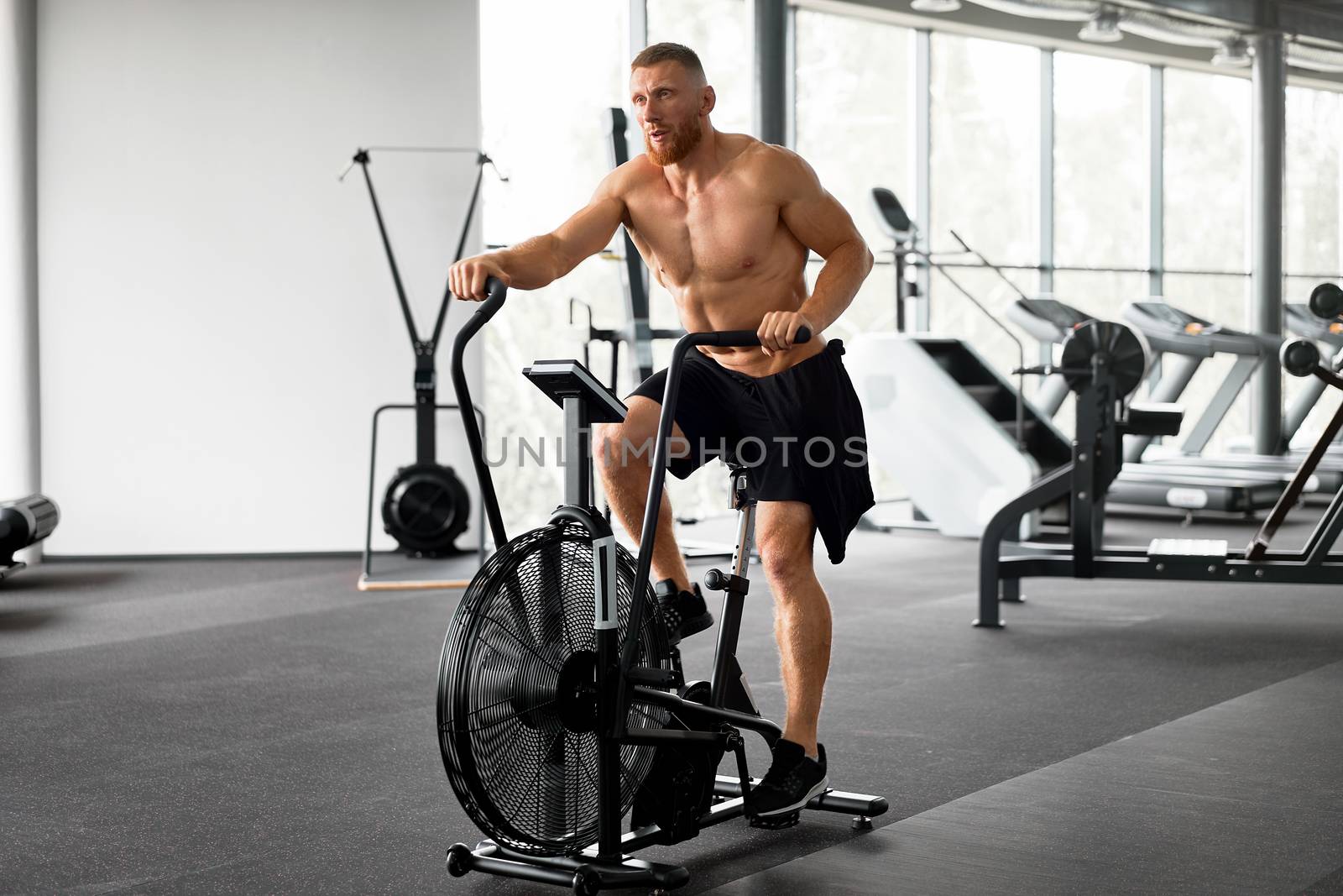 Man exercise bike gym cycling training fitness. Fitness male using air bike cardio workout. by andreonegin