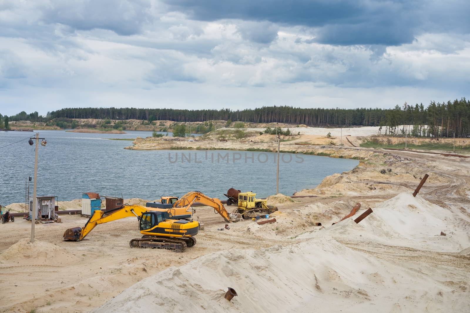 Sand quarry mining industry equipment excavator tractor standing sand land near lake water Industrial activity mine operation summer sunny day. Ecology problem Non-renewable resources of the Earth