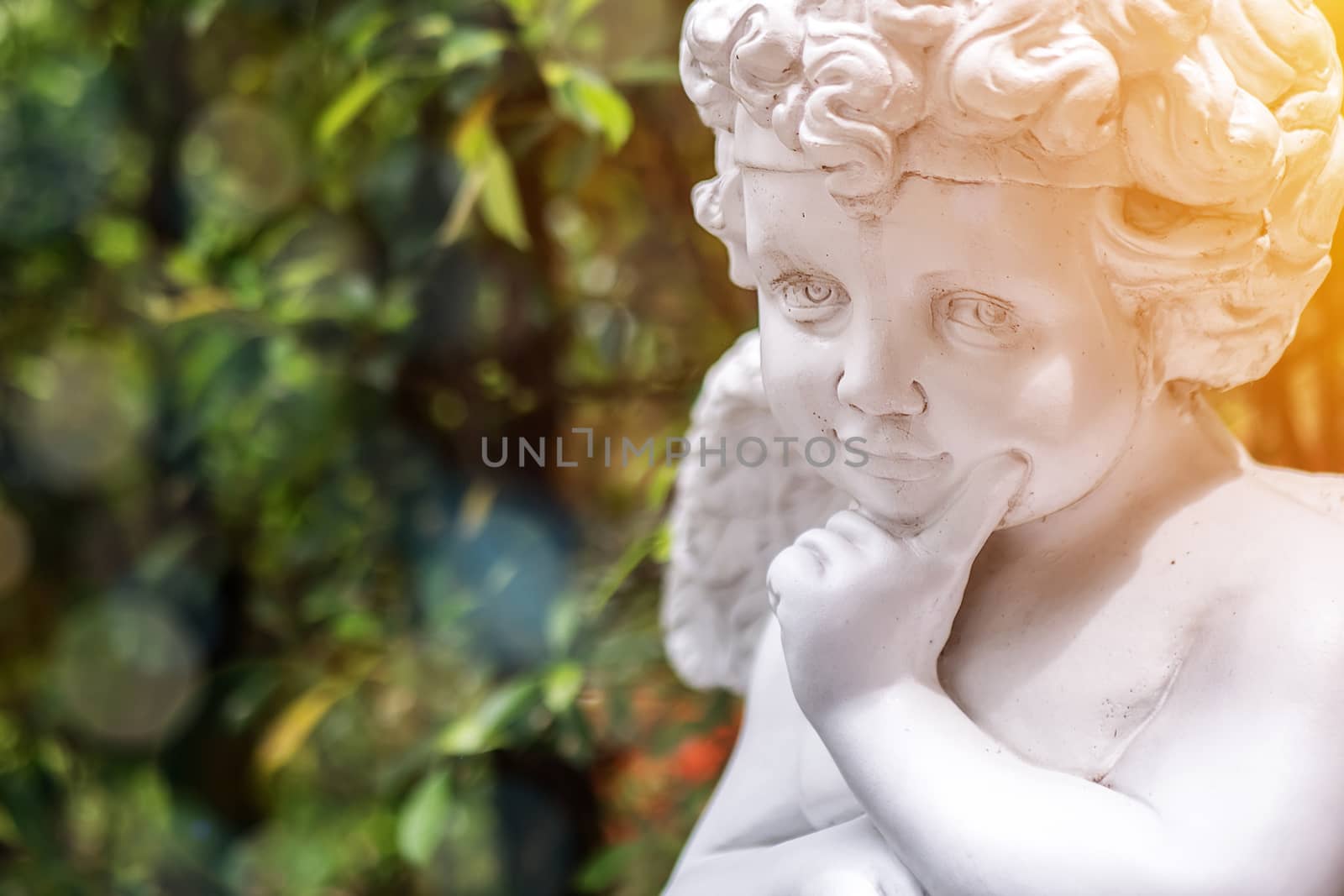 Garden decorate background concept. White vintage statue cupid in the garden with green copy space at the left side. Morning light , bokeh and lens flare effect. English style garden