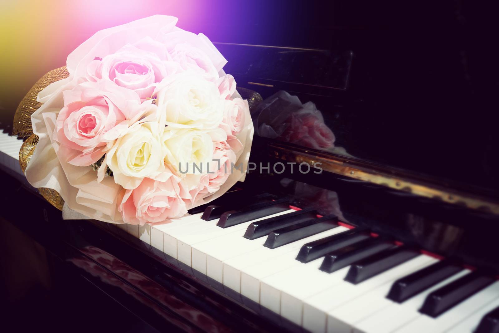 Rose flower in bouquet on keyboard of piano with light flare in concert performance. Selective focus image. Warm color tone music background