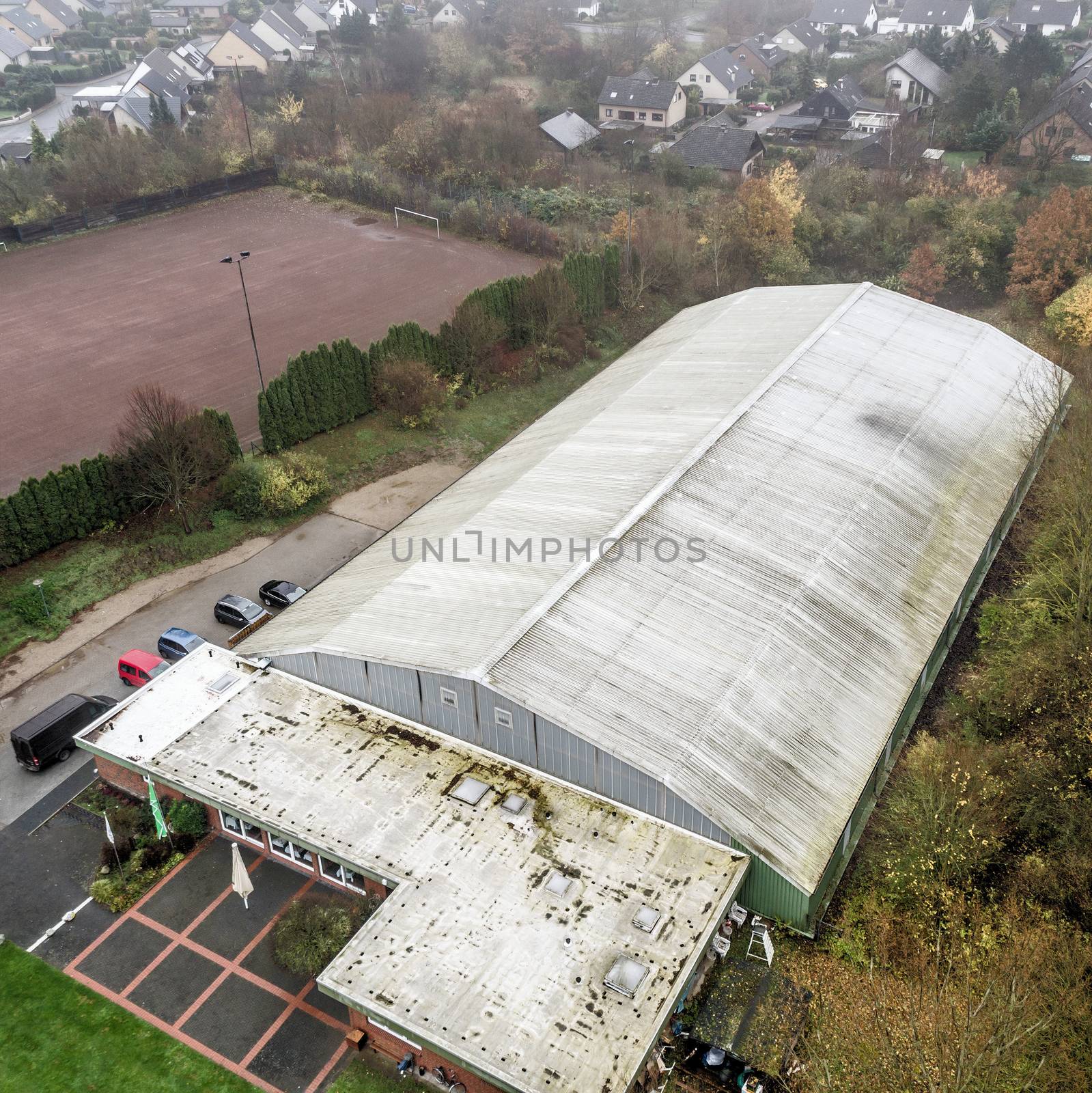 Aerial photo of an old ugly tennis hall with a residential area in the background, photo taken with the drone from a height of 50 meters.