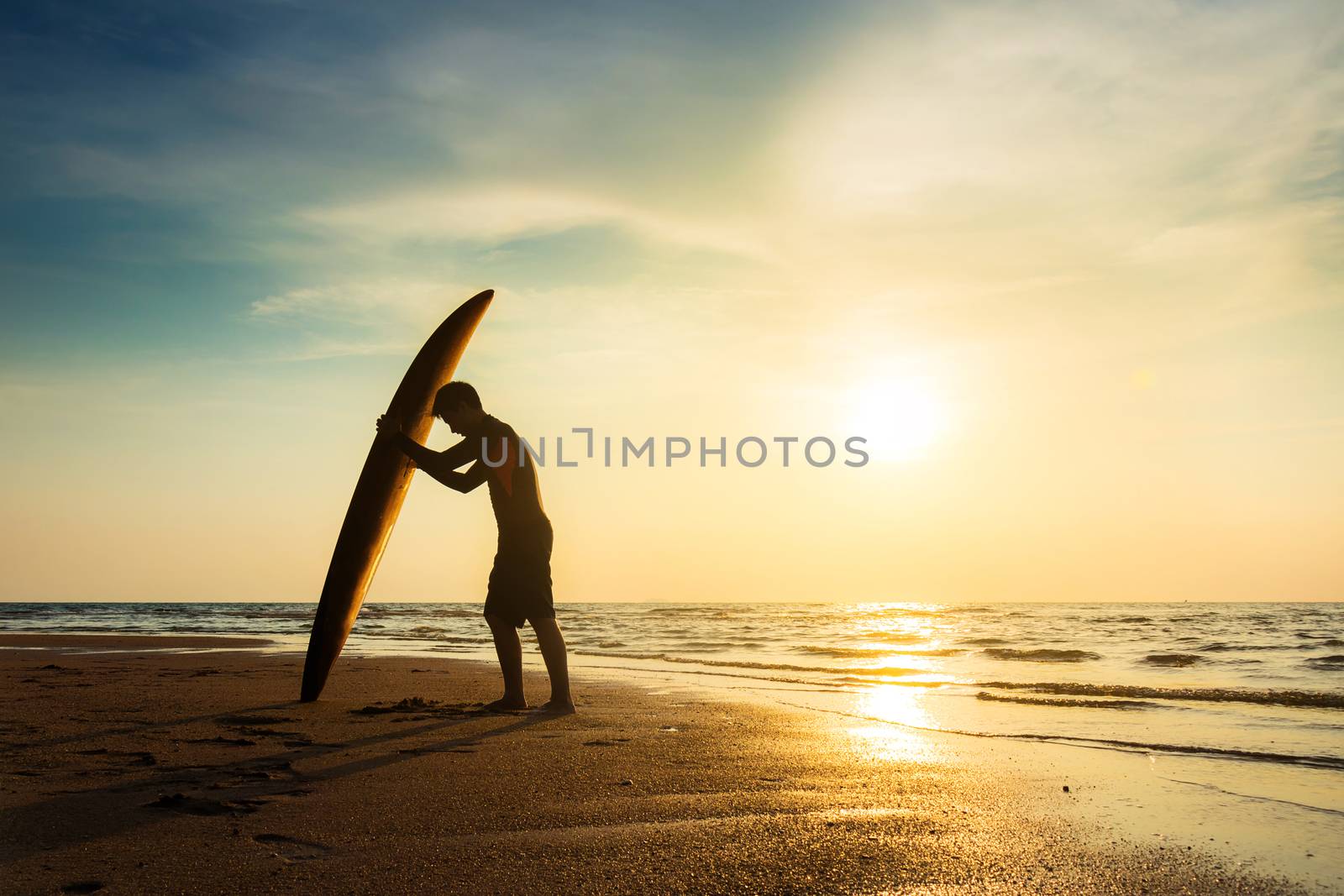Surfing for water sport outdoor activity lifestyle concept. Silhouette of young happy surf man at white beach with surfboard. Surfer on the beach in sea shore at sunset time with beautiful light.