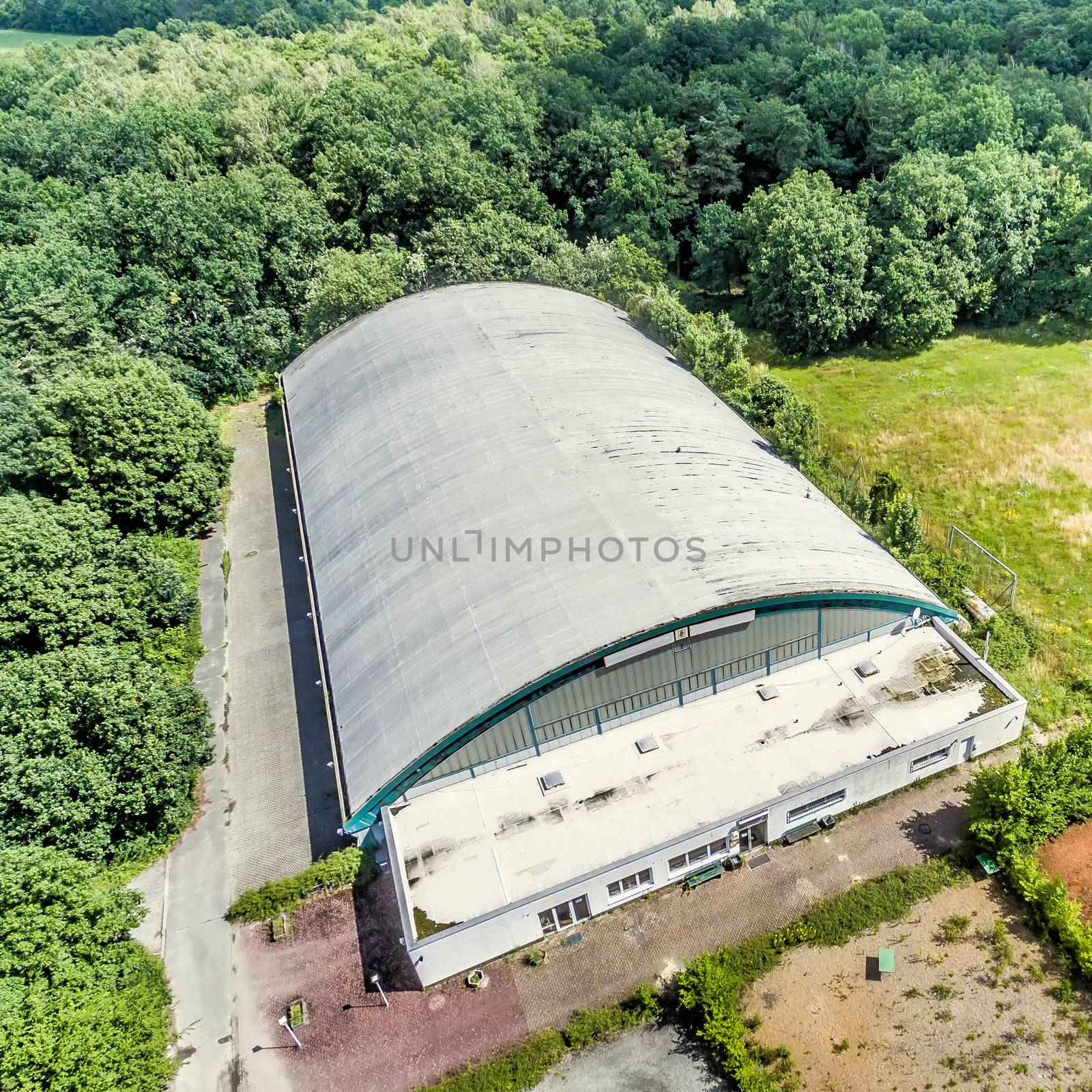 Obliquely photographed aerial view of an old tennis and soccer hall, forest in the surroundings