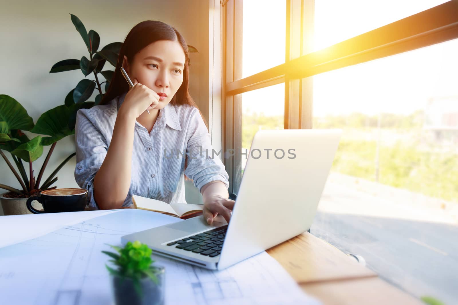 Serious Asian female architects working under pressure using laptop for researching the architectural analyze project sit near the window in modern home for freelance job. Asia model