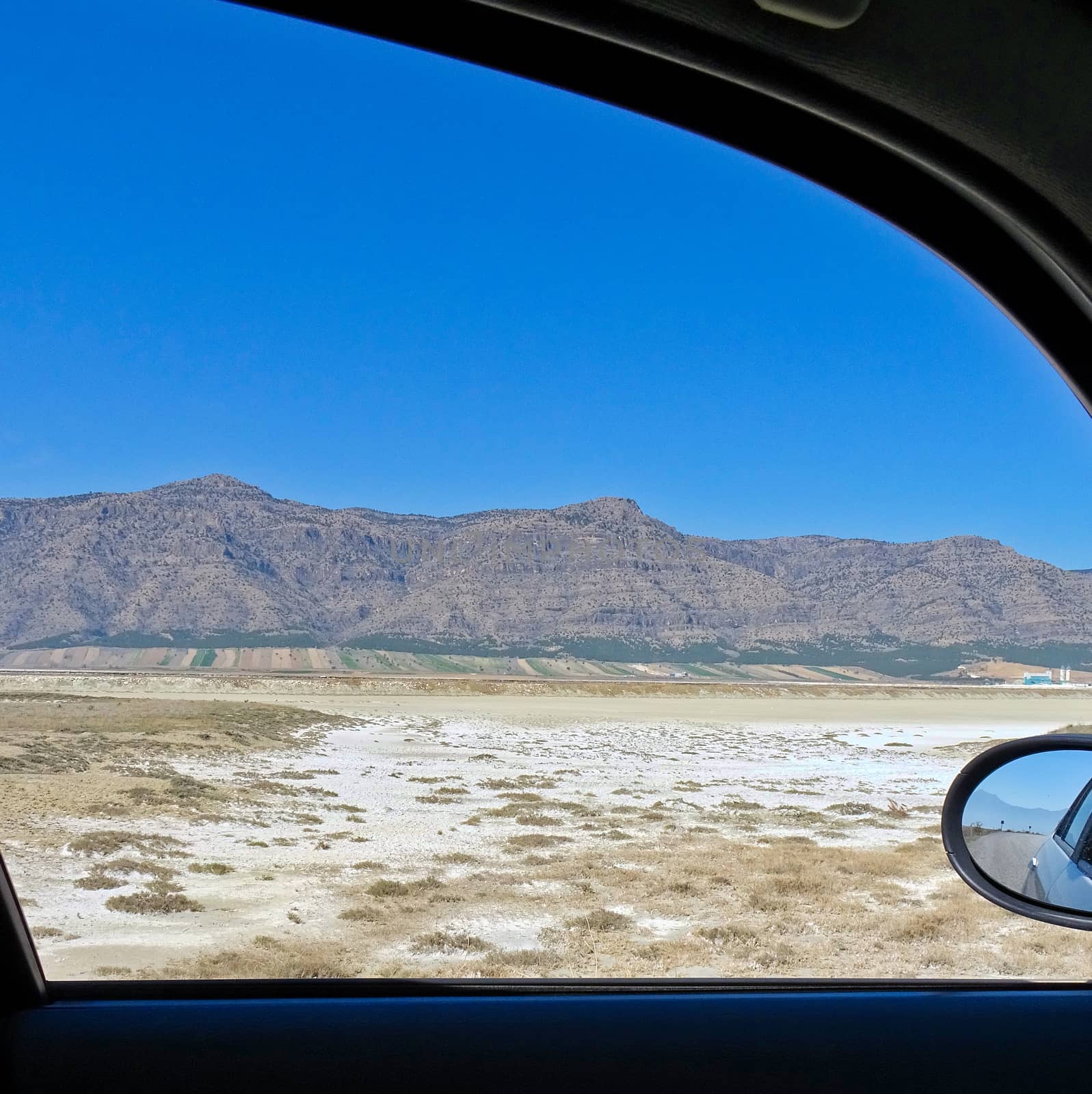 View from the window of a car to the semi-desert in Central Turkey with a salty depression in the foreground and bare rocks on the horizon, blue sky