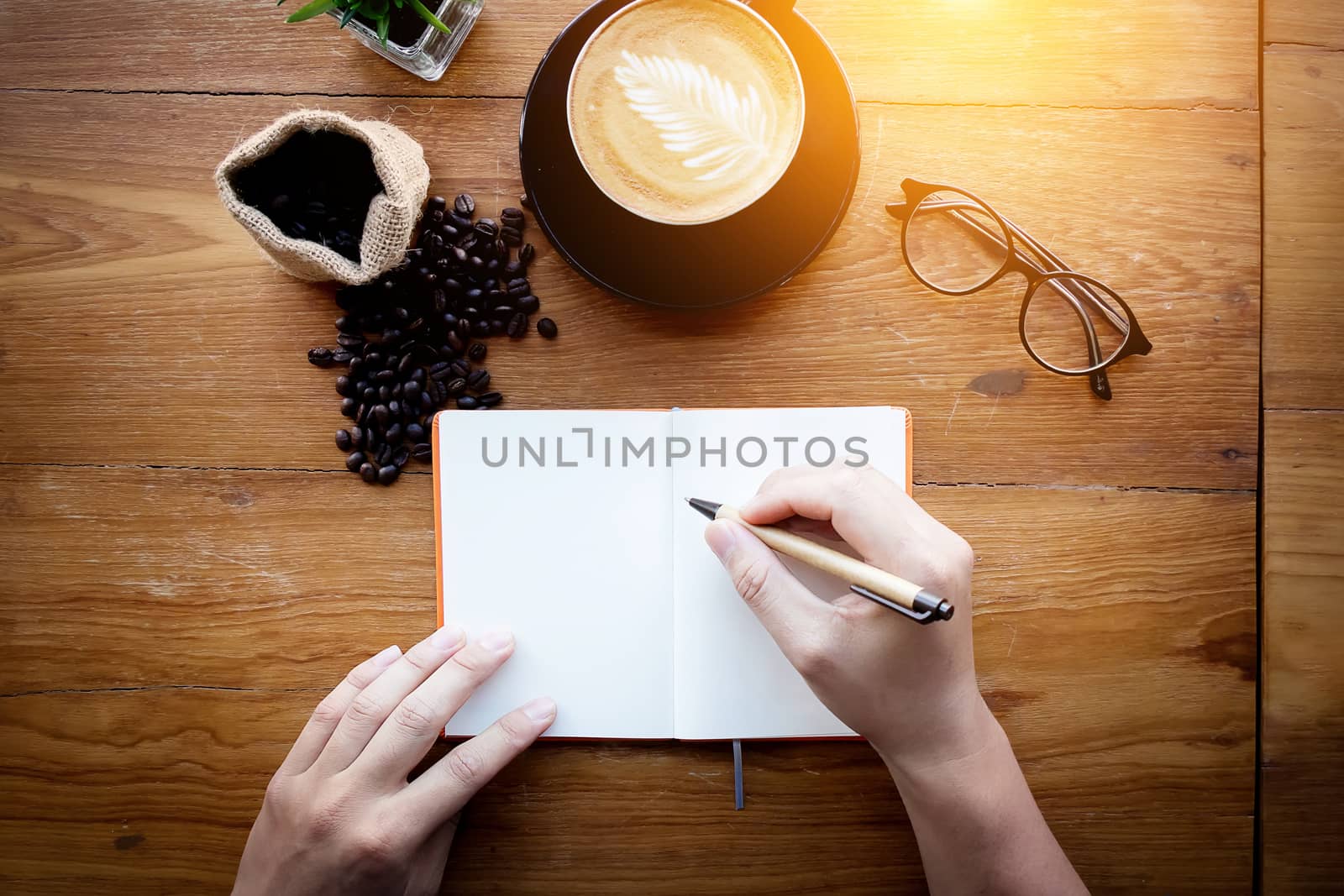 Barista cafe making coffee preparation service. Man holding a pen writing note on empty white page with space for text on vintage office desk decoration with cappuccino coffee and coffee bean,top view by asiandelight