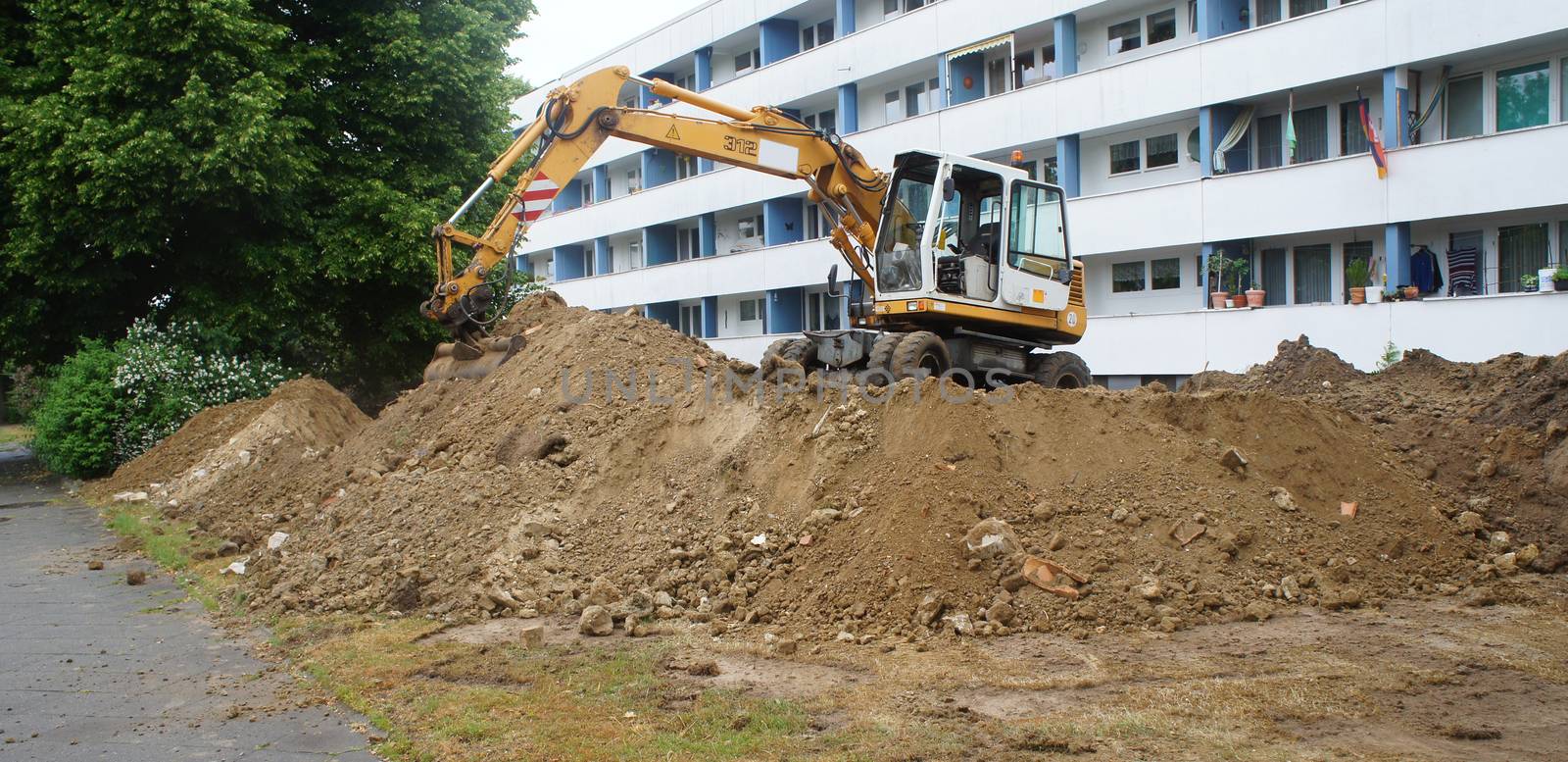 Construction site for the laying of new canals and pipes in front of a large, ugly apartment building with lots of cheap apartments, construct