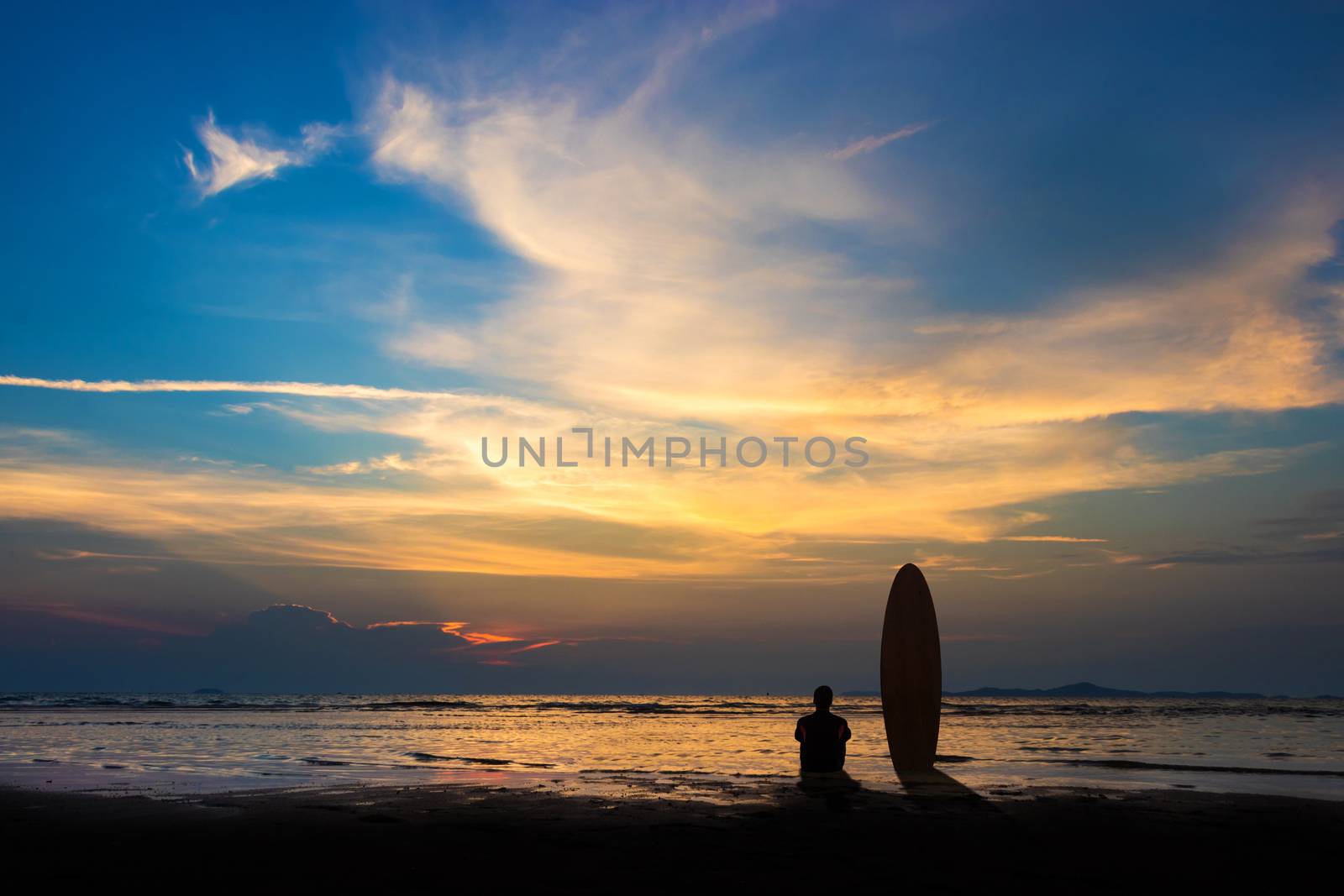 Silhouette of surf man sit with a surfboard on the beach. Surfing scene at sunset beach with colorful sky. Outdoor water sport adventure lifestyle.Summer activity. Handsome Asia male model in his 20s.