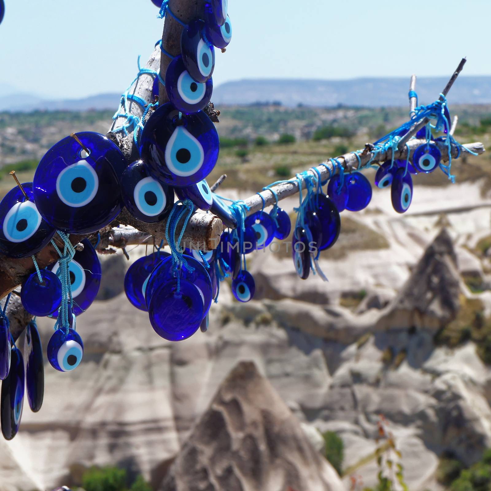 The blue glass eye (Nazar Boncugu) as a defence against the evil eye, at a branch in front of the mountains of Cappadocia, closeup