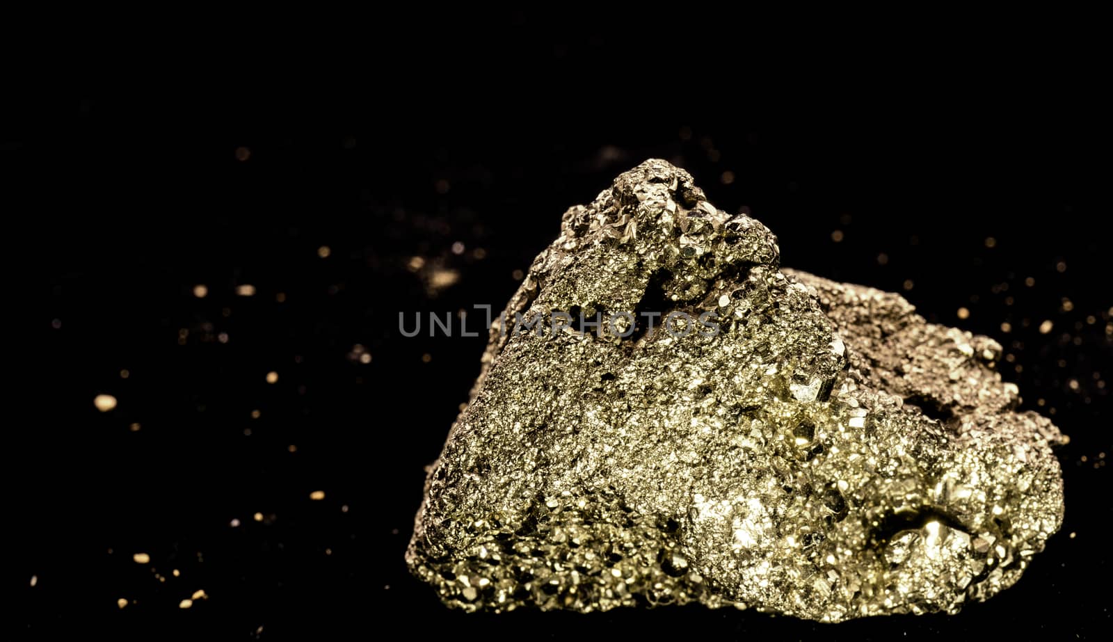 Cubic pyrite crystal stone, cat gold, in front of a black background with blurred fragments at a distance, macro