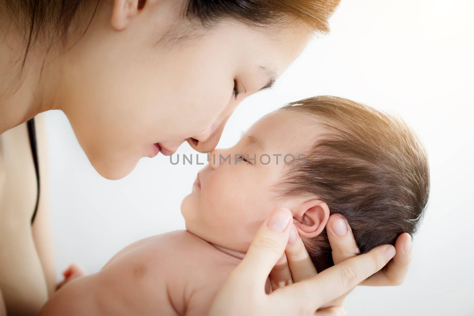 Concept of love and family relationship : Portrait of happy Asian mother use nose touch newborn cute little baby nose on a white bed at home. Parent and little kid relaxing hug and kiss at home. by asiandelight