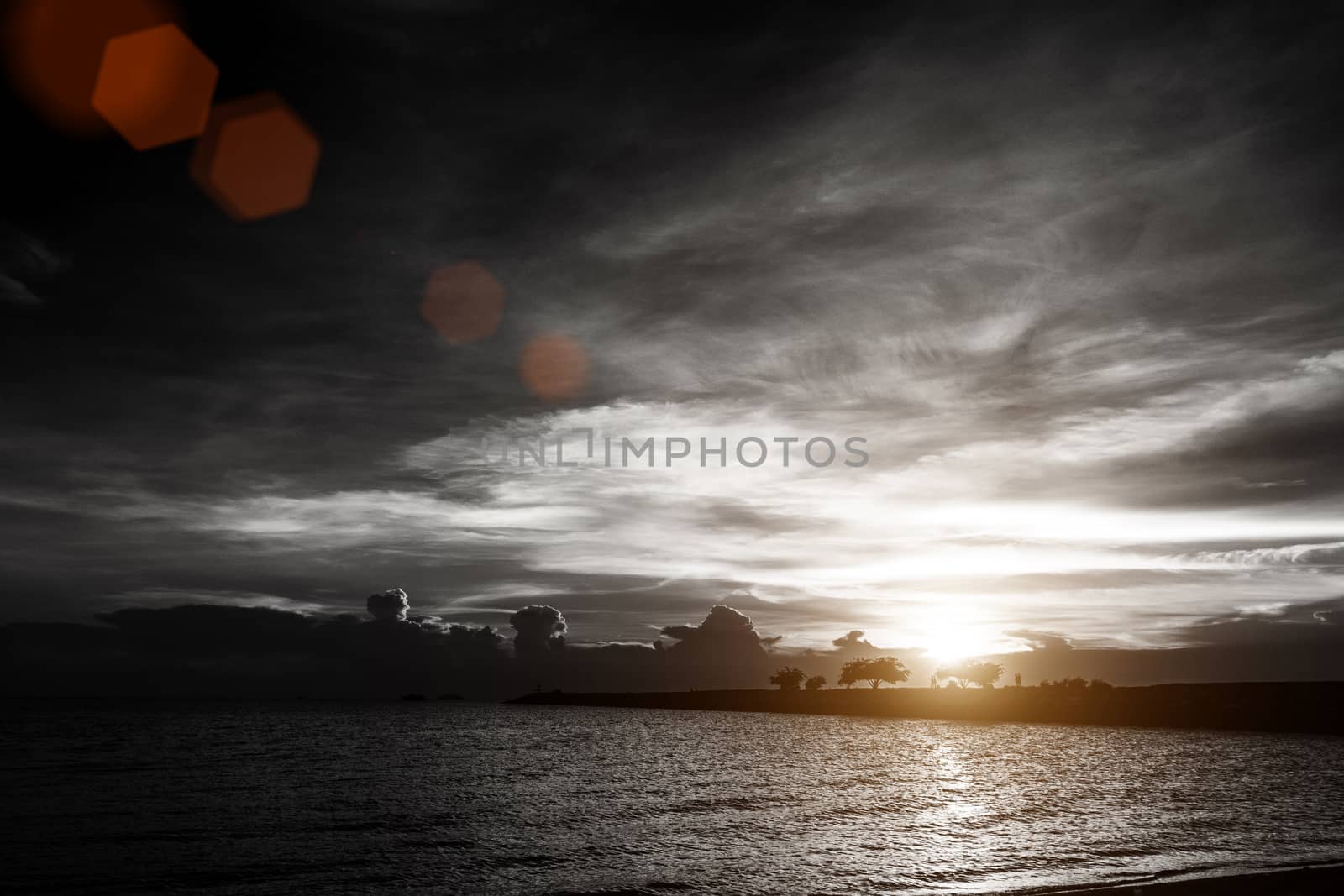 sunset on cloudy sky at the sea beach with silhouette rock bridge and tree background , black and white color with red lens flare effect