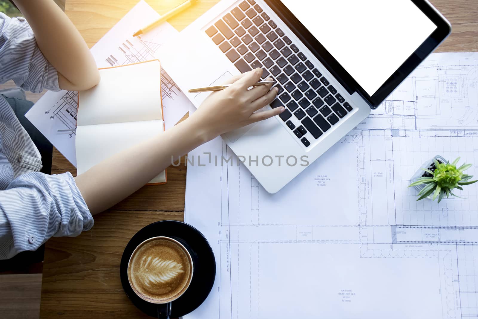 architect , engineering , creative and designer workspace concept : Top view of Asian female architect working with blueprint , notebook and laptop on architectural project , anonymous face.