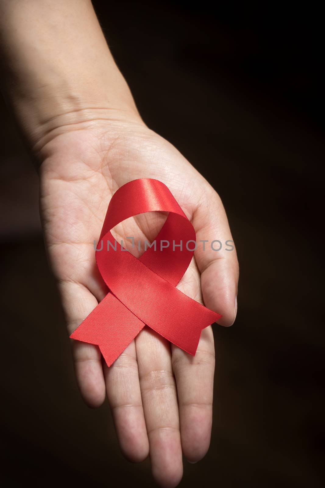 World AIDS Day concept : Red ribbon on human hand isolate on black background. Red ribbon symbolic bow color raising awareness on World AIDS Day , 1 December by asiandelight