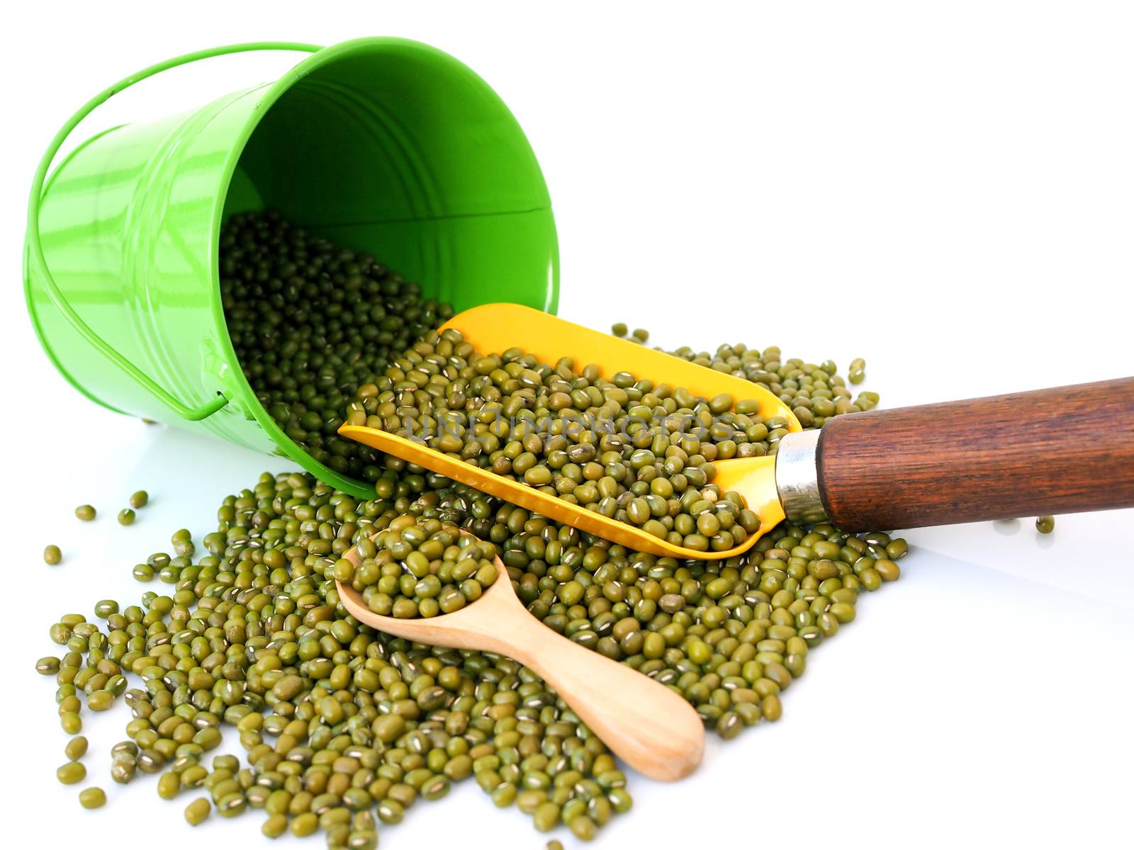 Above of yellow shovel used to scoop green mung beans in bucket, isolated on white background.