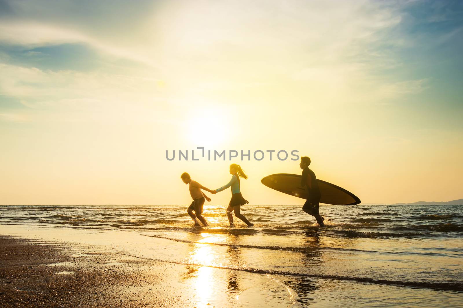Outdoor sport activity friendship concept : Silhouette of group of young joyful surfer friend running into the sea with surf boards on sunset beach by asiandelight