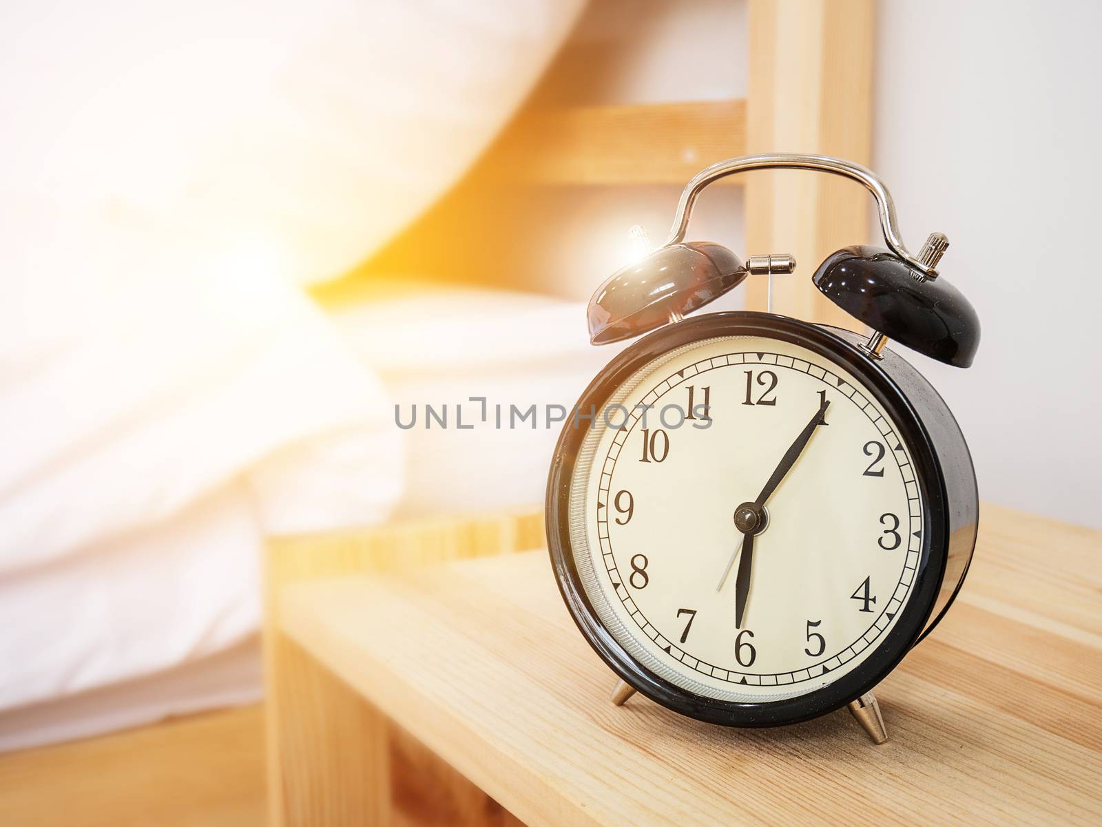 Alarm clock , wake-up time concept : Retro alarm clock with five minutes past six o'clock in the morning on wooden bed side table with white bed sheet and morning sunlight background