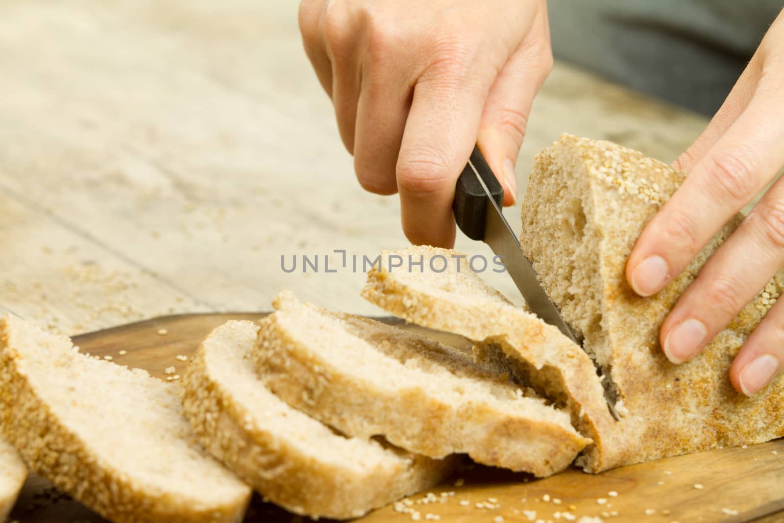 Close up of woman hands slicing a loaf of homemade bread with se