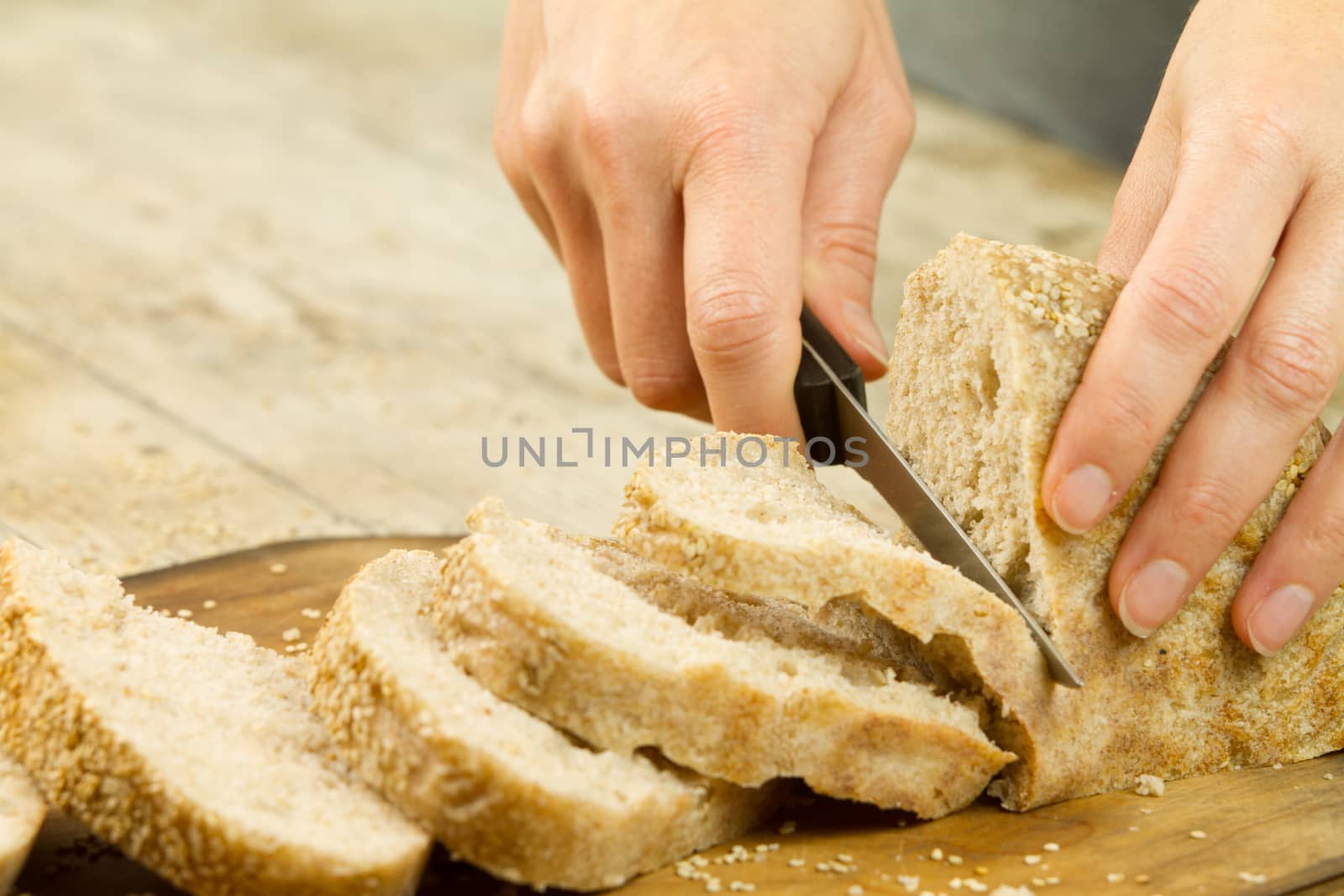 Close up of woman hands slicing a loaf of homemade bread with se by robbyfontanesi