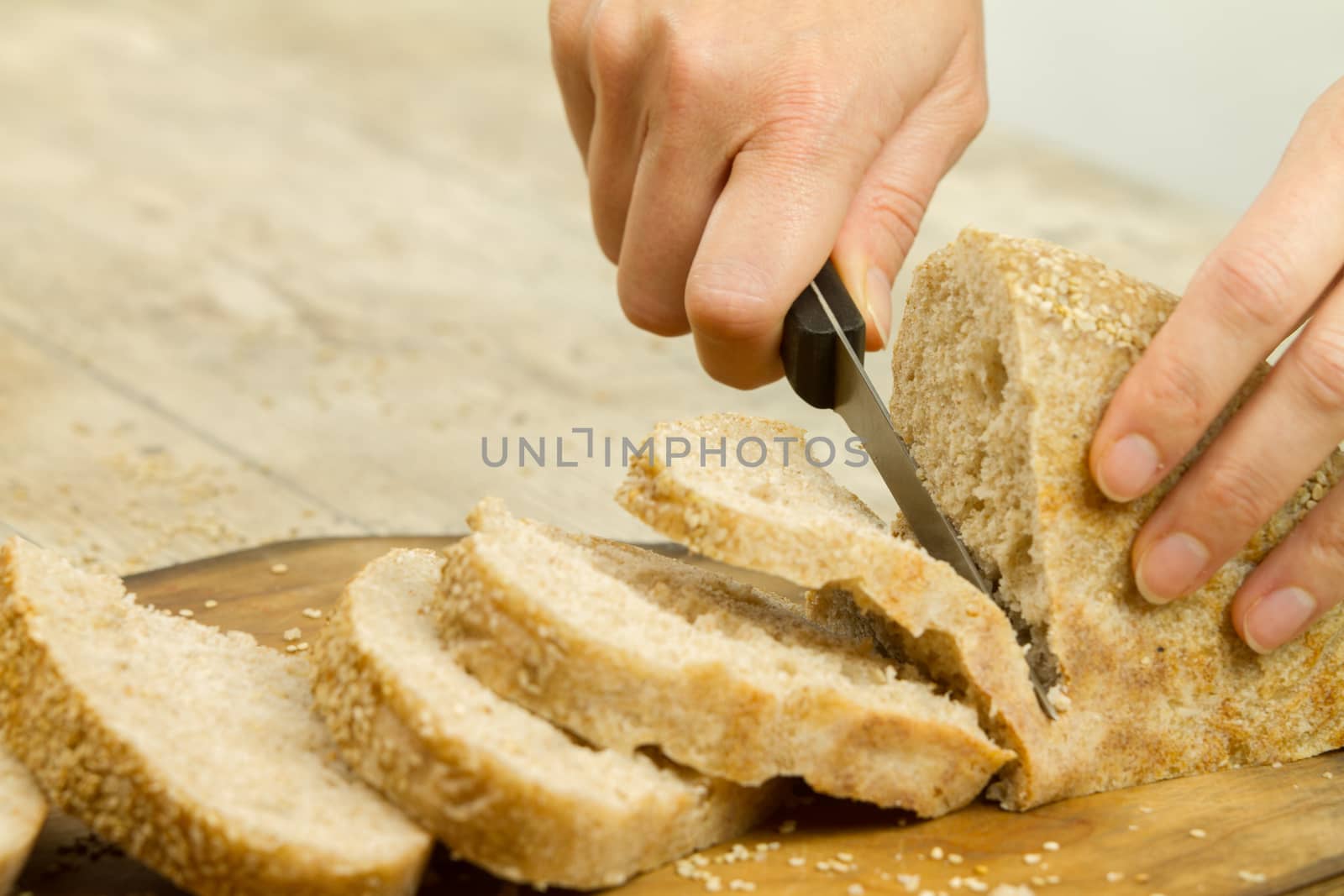 Close up of woman hands slicing a loaf of homemade bread with se by robbyfontanesi