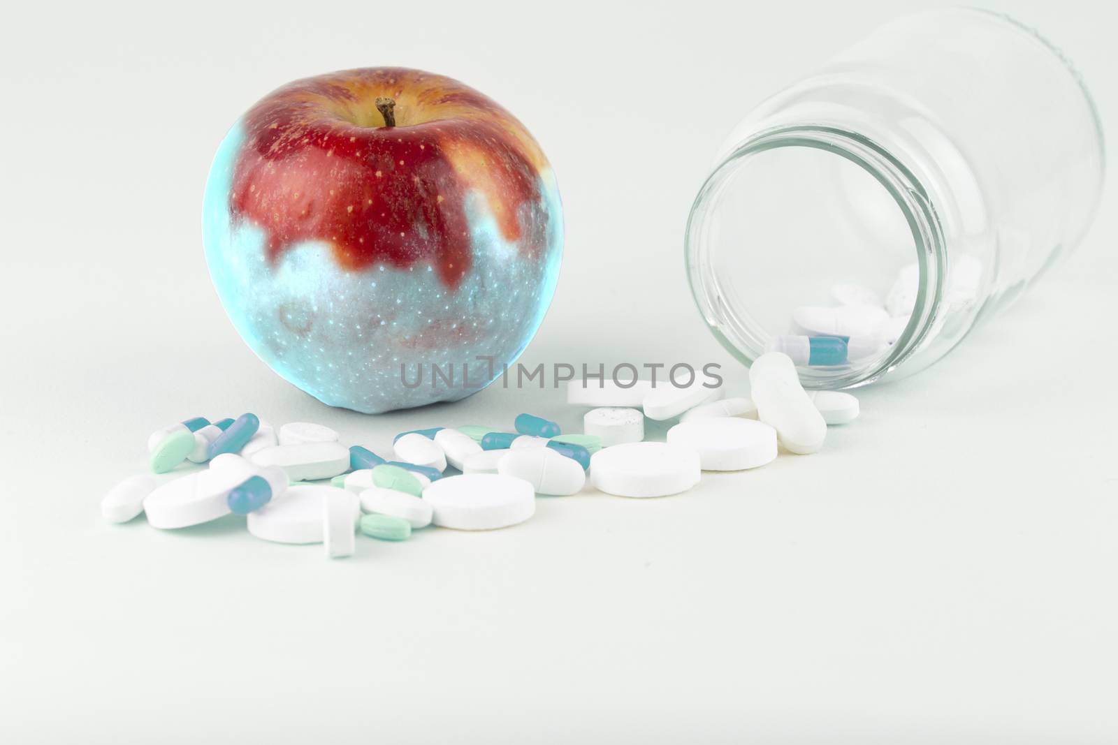 Concept: human GMO manipulation of nature and relative poisoned fruits. Close-up of an apple contaminated by changing color from the medicines in front of it on a white background