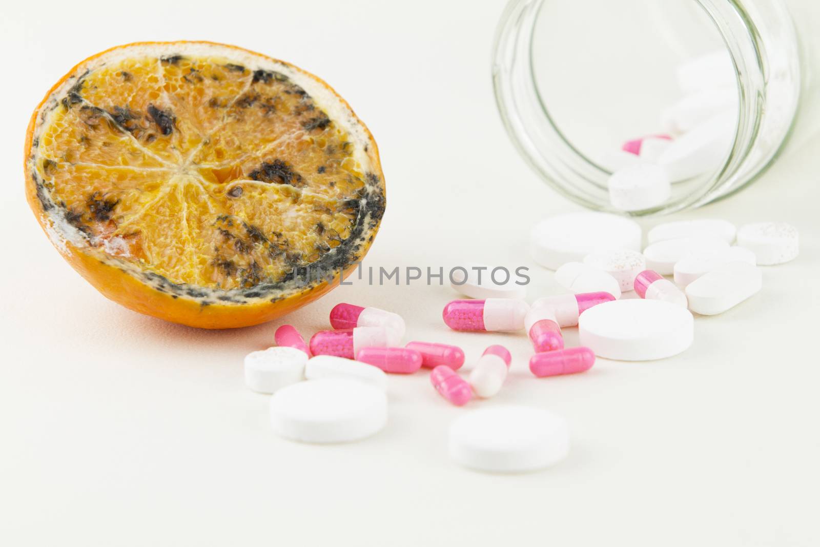 Concept: human GMO manipulation of nature and relative poisoned fruits. Close-up of an half orange contaminated by changing color from the medicines in front of it on a white background